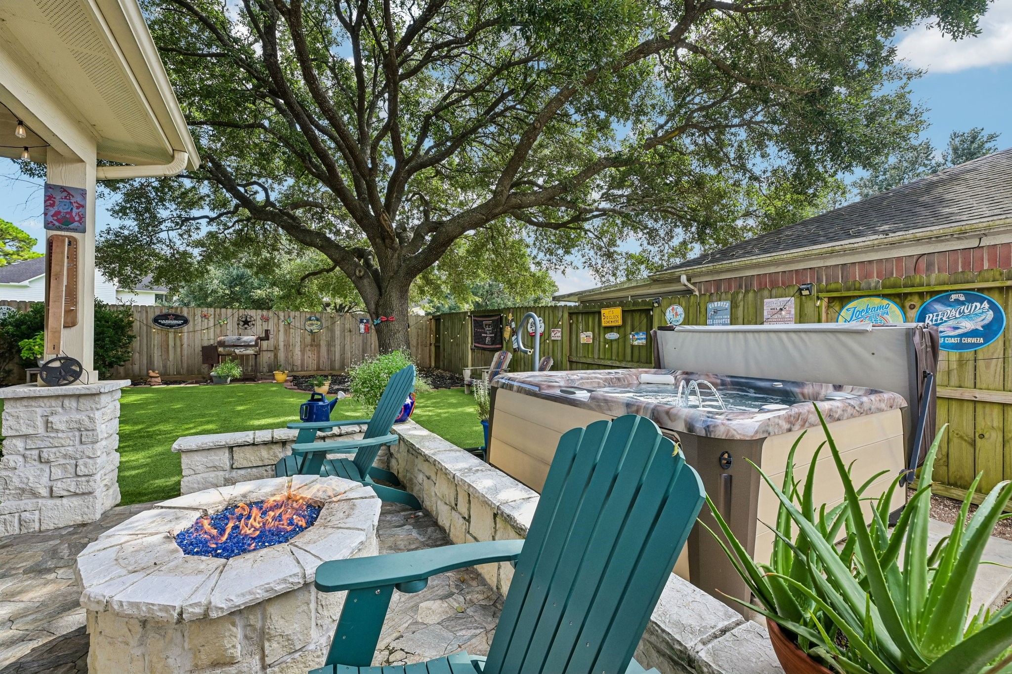 Stone-built outdoor fire pit area with blue glass fire media and Adirondack seating positioned right next to the hot tub.