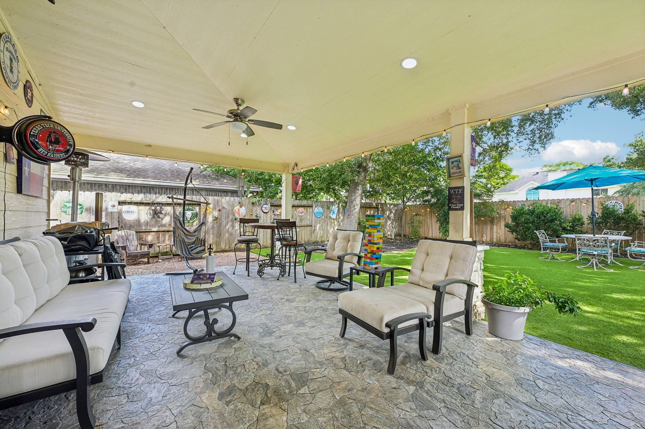 Generous covered lounge area offering comfortable outdoor sofa seating, coffee table, ceiling fan, and seamless connection to the backyard turf and green space.