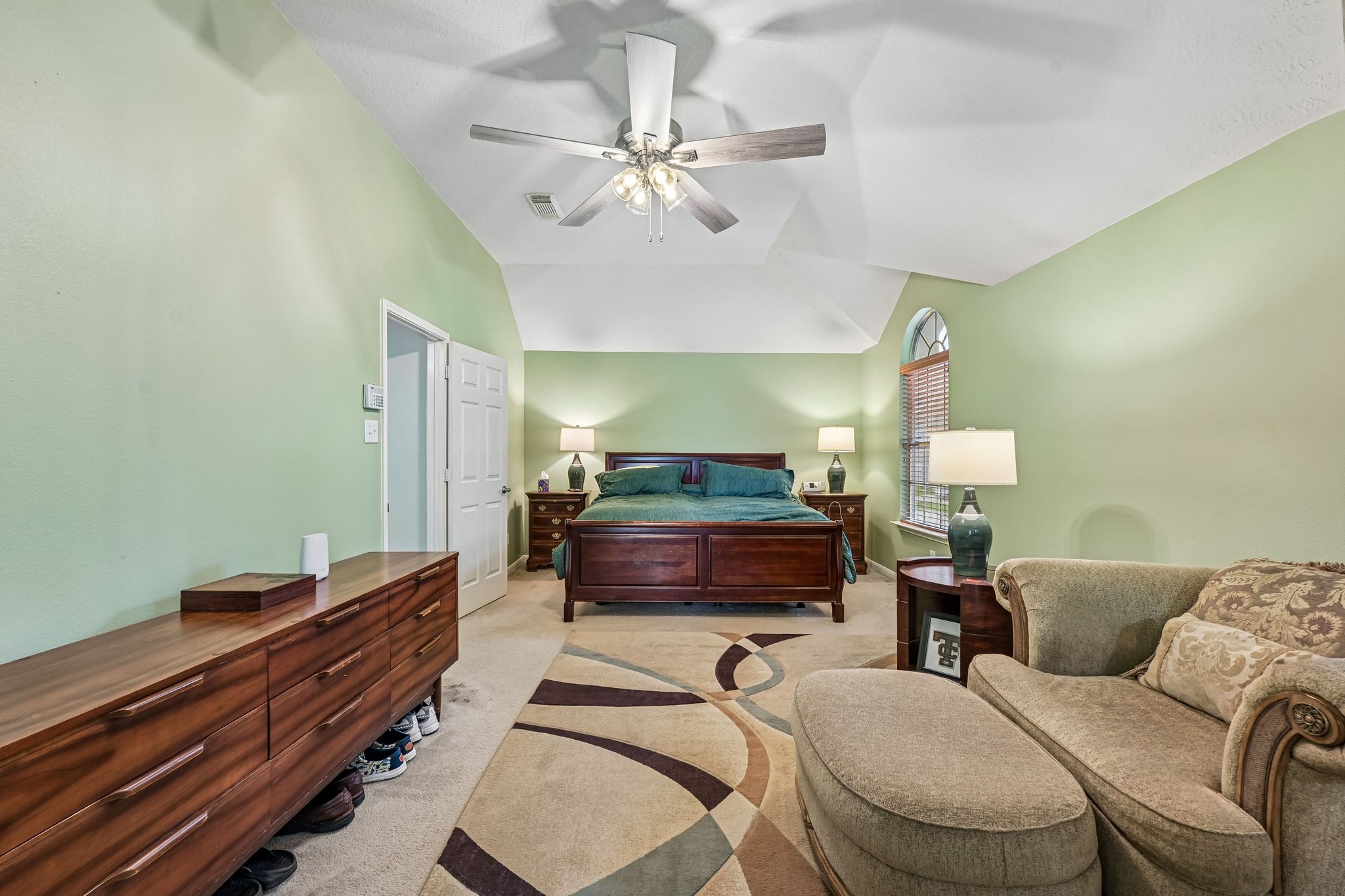Primary bedroom suite showcasing vaulted ceilings, ceiling fan, generous floor space for large furniture, and en-suite access.
