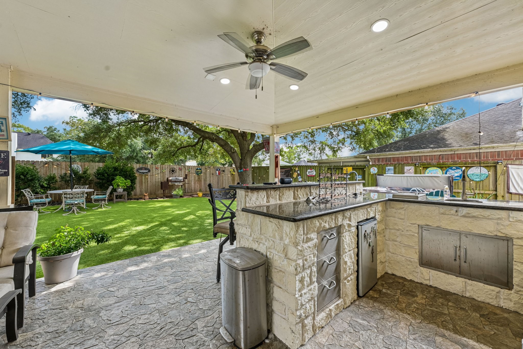 Fully equipped outdoor kitchen built with stone masonry, granite countertops, built-in stainless steel appliances, storage drawers, and a raised bar counter