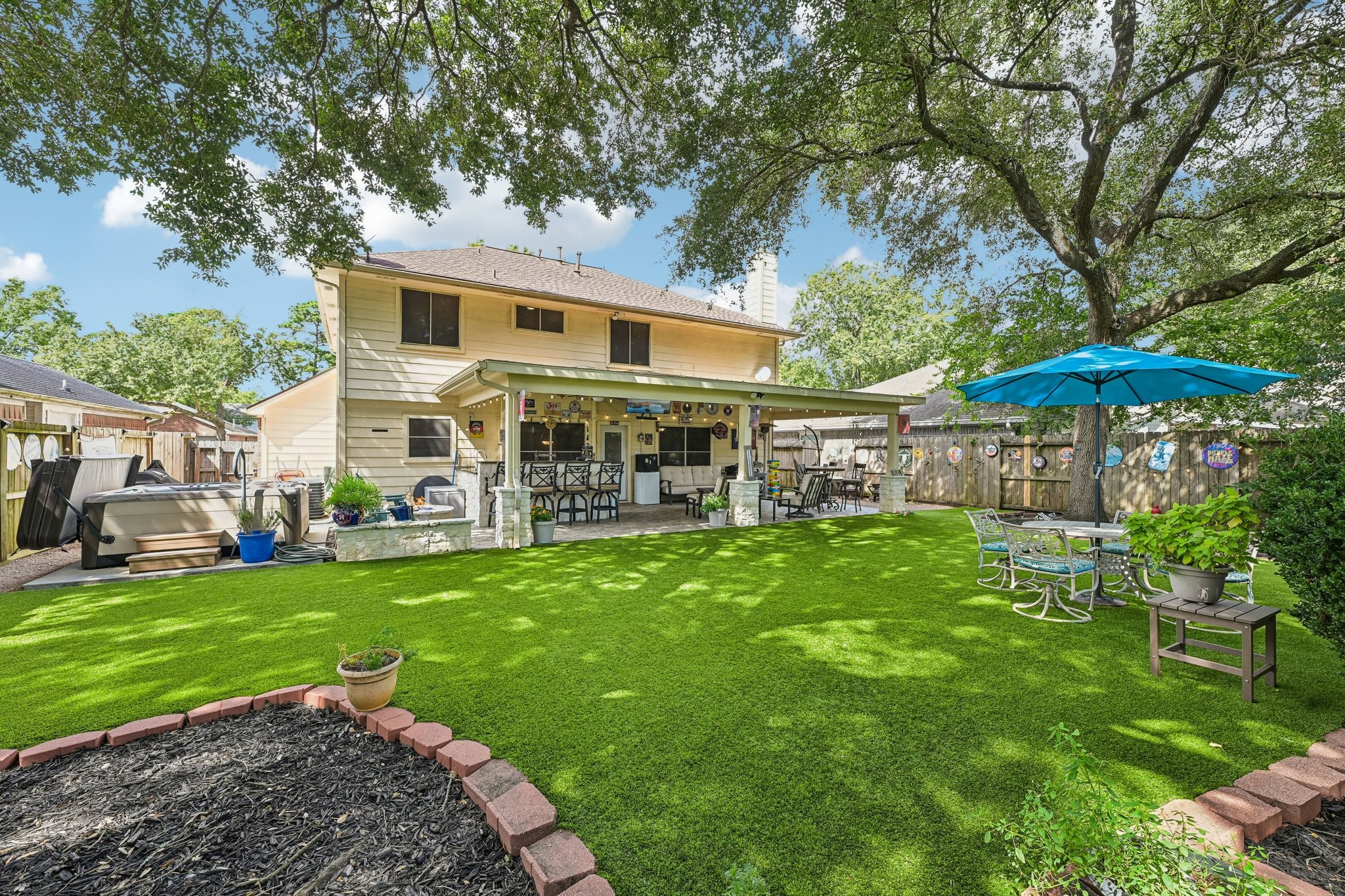 Overview of the ultimate backyard oasis showcasing the extensive covered patio, lush artificial turf lawn, custom putting green, and mature shade trees.