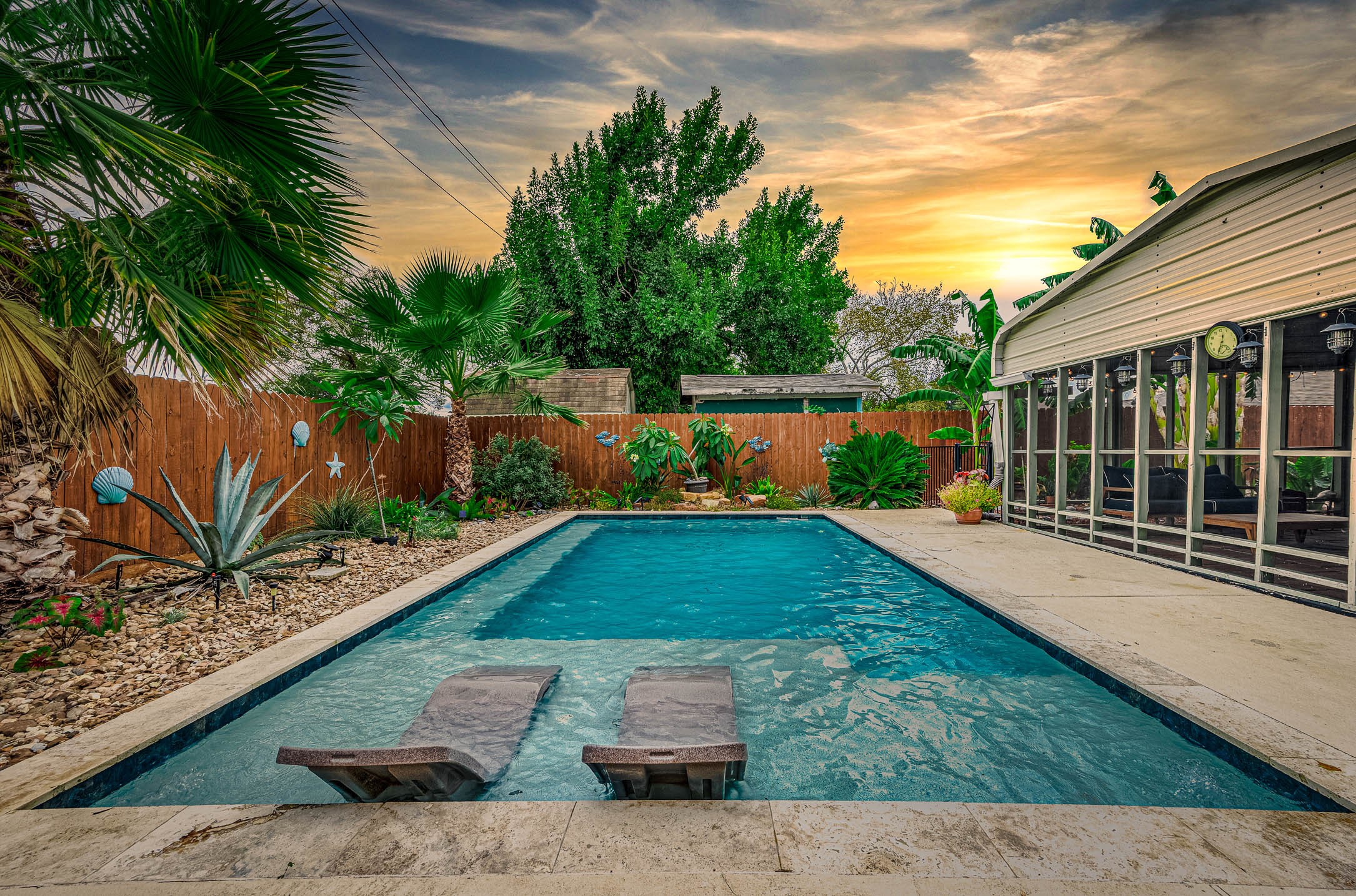 In-ground gunite pool with tanning ledge, surrounded by lush tropical landscaping.