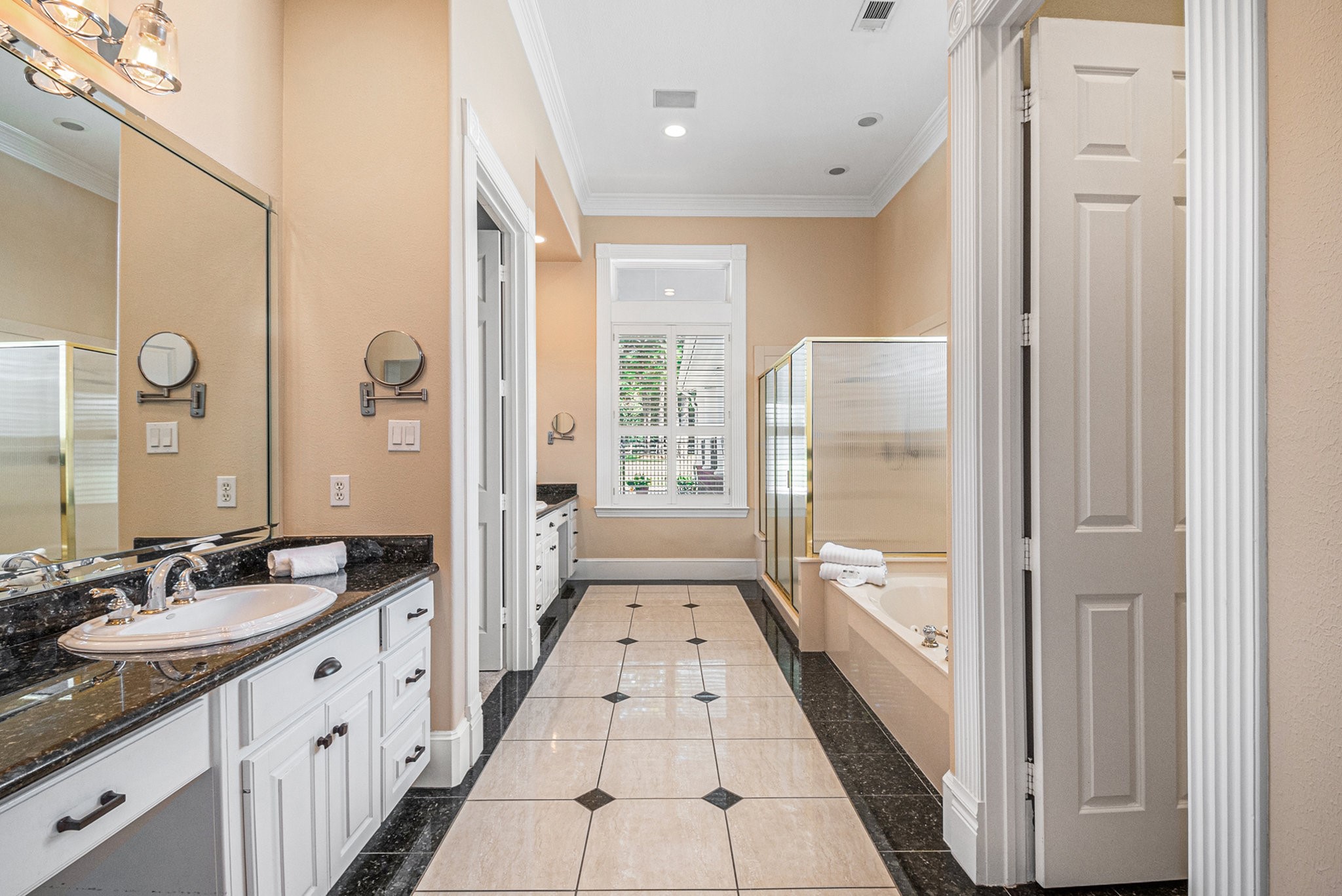 Magnificent primary bathroom features dual vanities with vanity seating, a glass-standing shower, a soaking tub, and a massive walk-in closet.