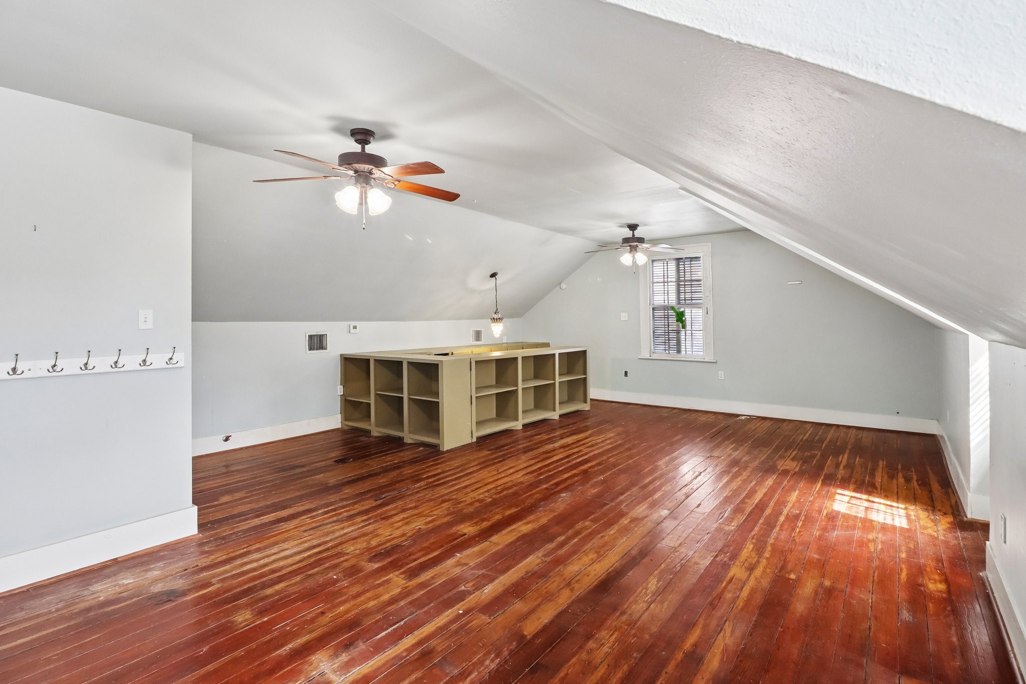 A bright upper-level room with wood flooring, a ceiling fan and windows beneath the sloped ceiling.