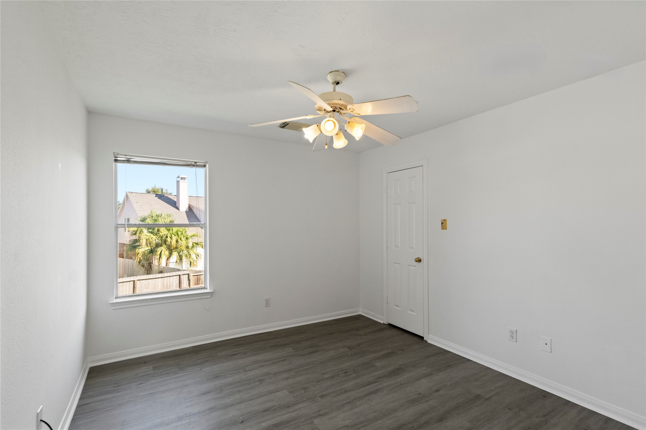 Bedroom 2 features modern gray flooring, a ceiling fan, and a window that fills the space with natural light.