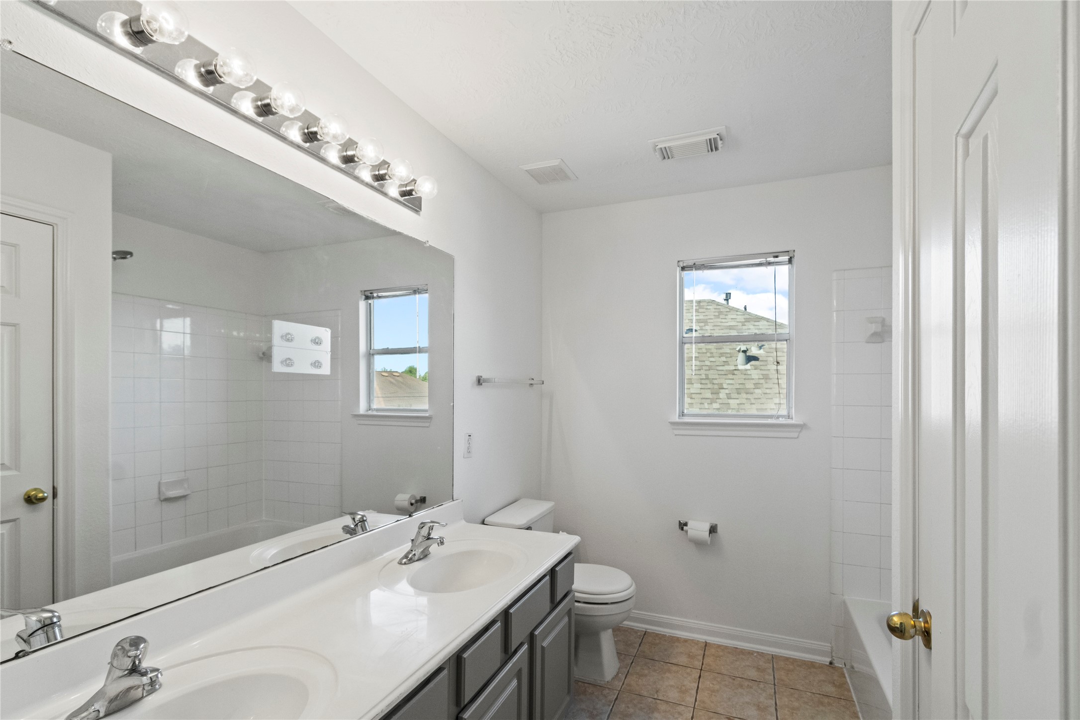Double-sink vanity bath with tub/shower combo, tile floors, and bright natural light, conveniently located between bedrooms 3 and 4.