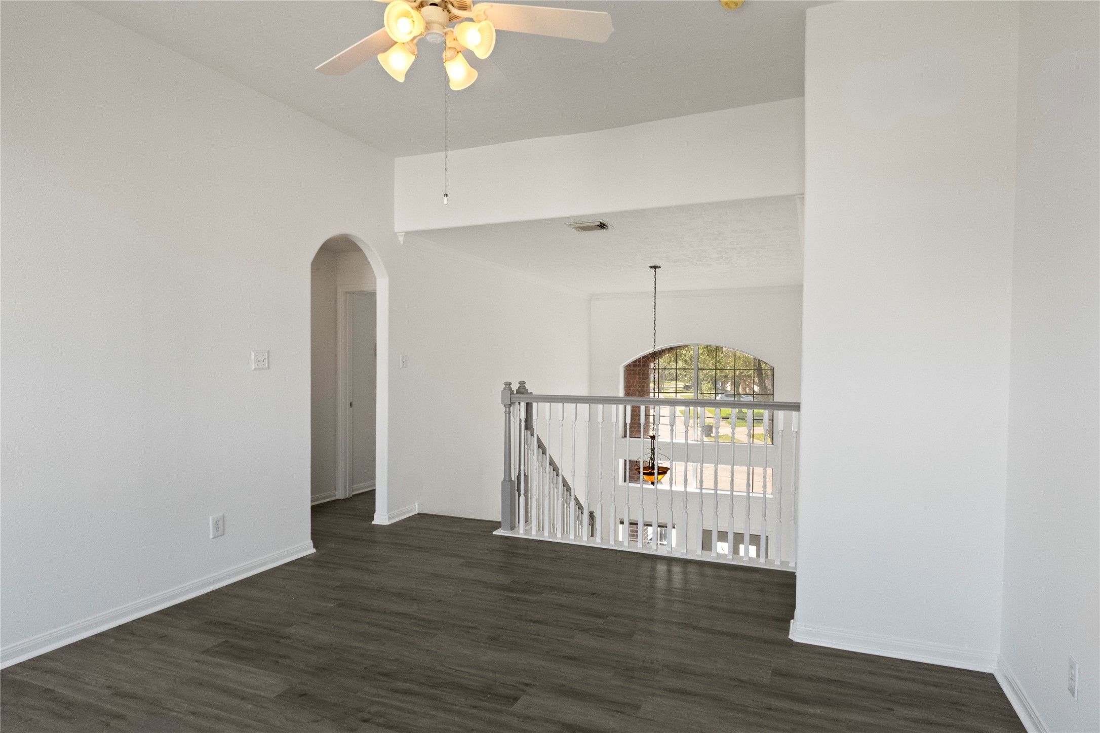 Spacious upstairs landing featuring dark wood-look flooring, a ceiling fan, and an open view overlooking the entryway with an elegant arched window.