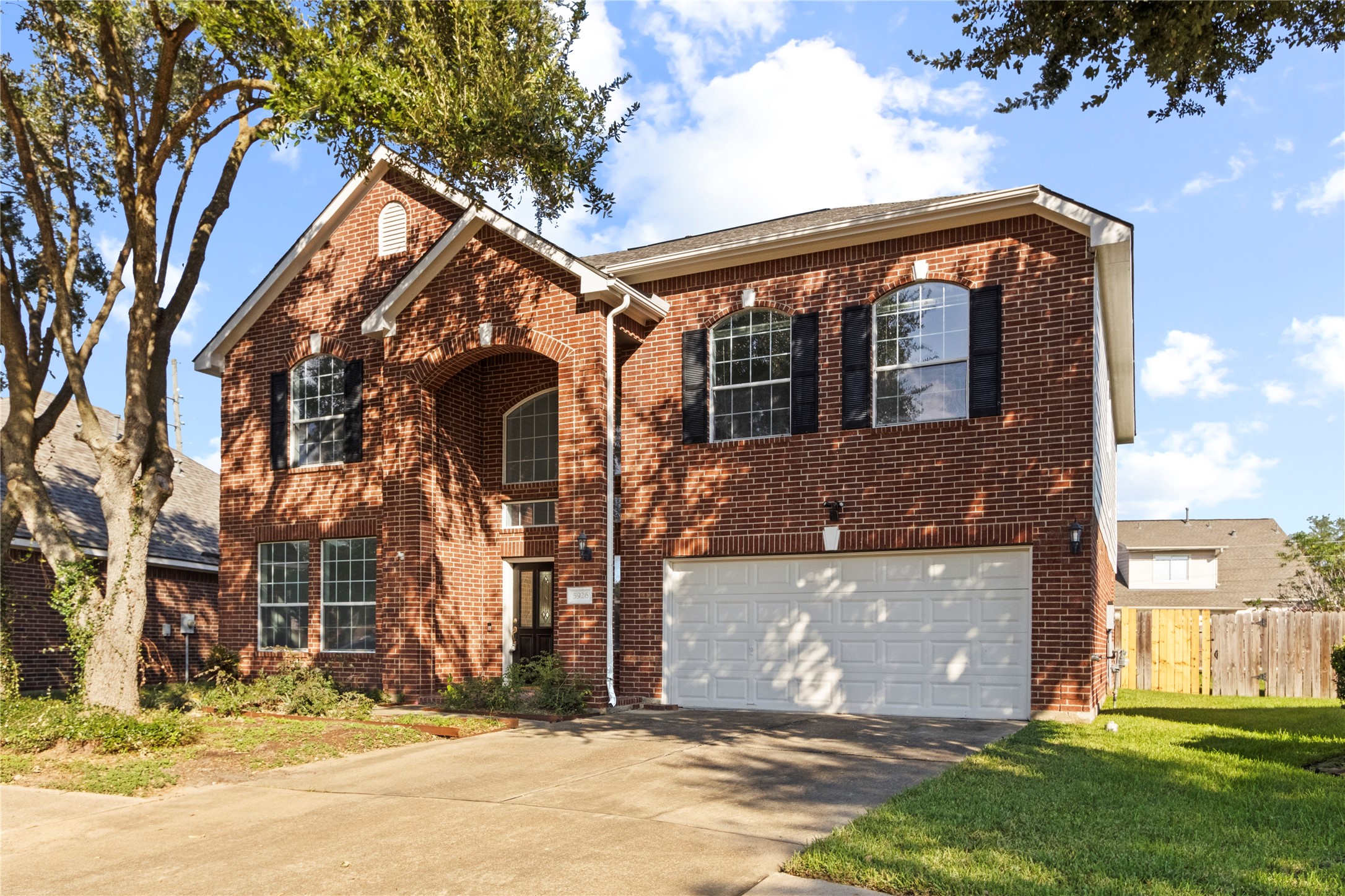 Two-story, red brick home featuring an arched front entry, large windows with black shutters, and an attached two-car garage. The covered entry and landscaped front yard add to the home's curb appeal. Two-story, red brick home featuring an arched front entry, large windows with black shutters, and an attached two-car garage. The covered entry and landscaped front yard add to the home's curb appeal.
