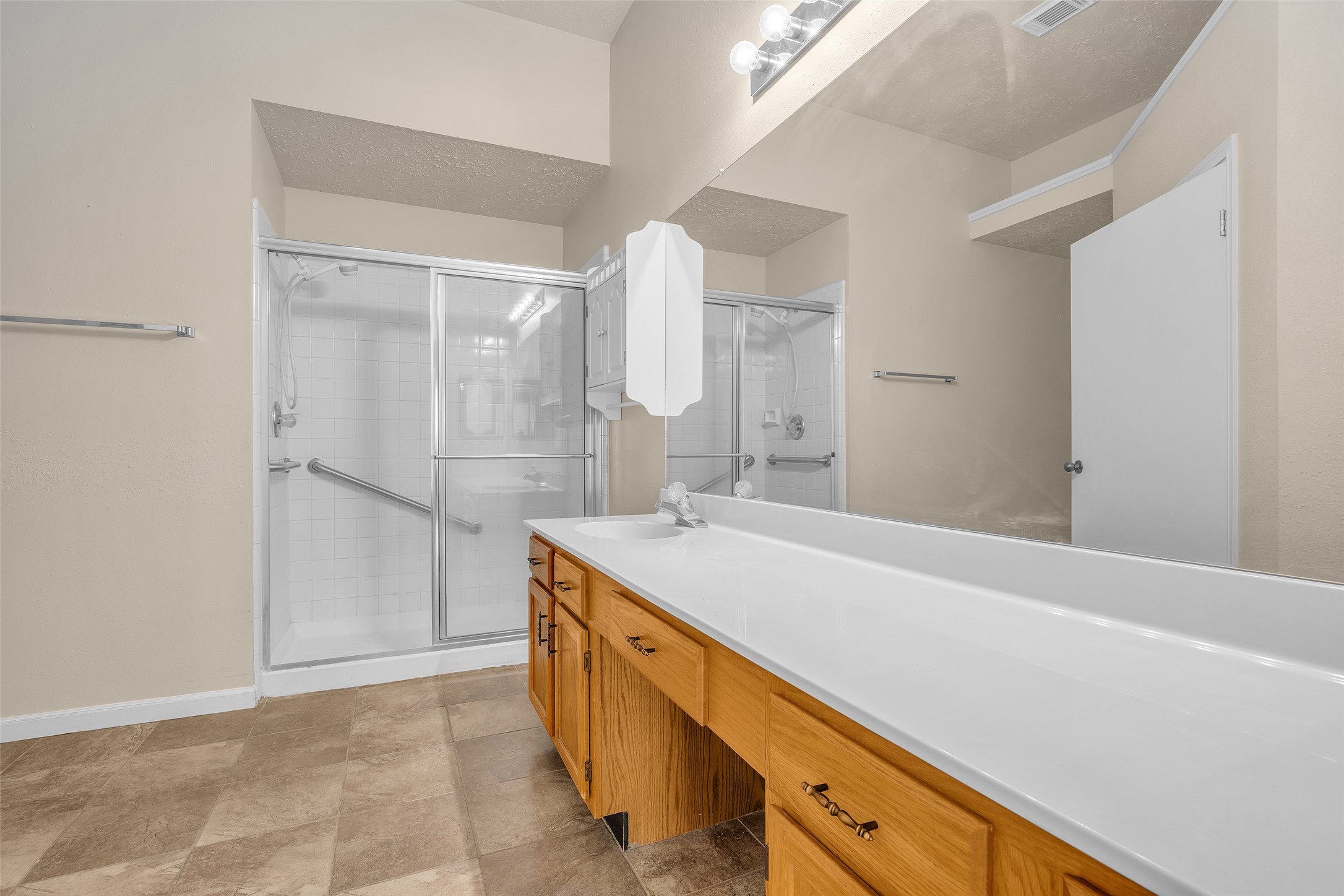 Primary bathroom features ample counter space, a vanity area with laminate countertops, and an enclosed shower, offering a clean, functional layout designed for everyday use.