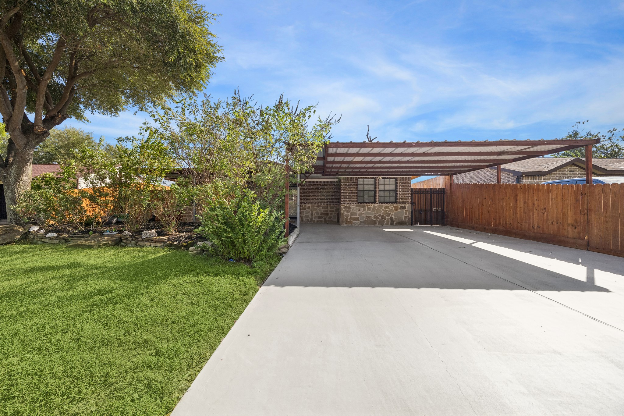 Spacious driveway with a covered carport, complemented by a lush green lawn and mature trees for added privacy and shade.