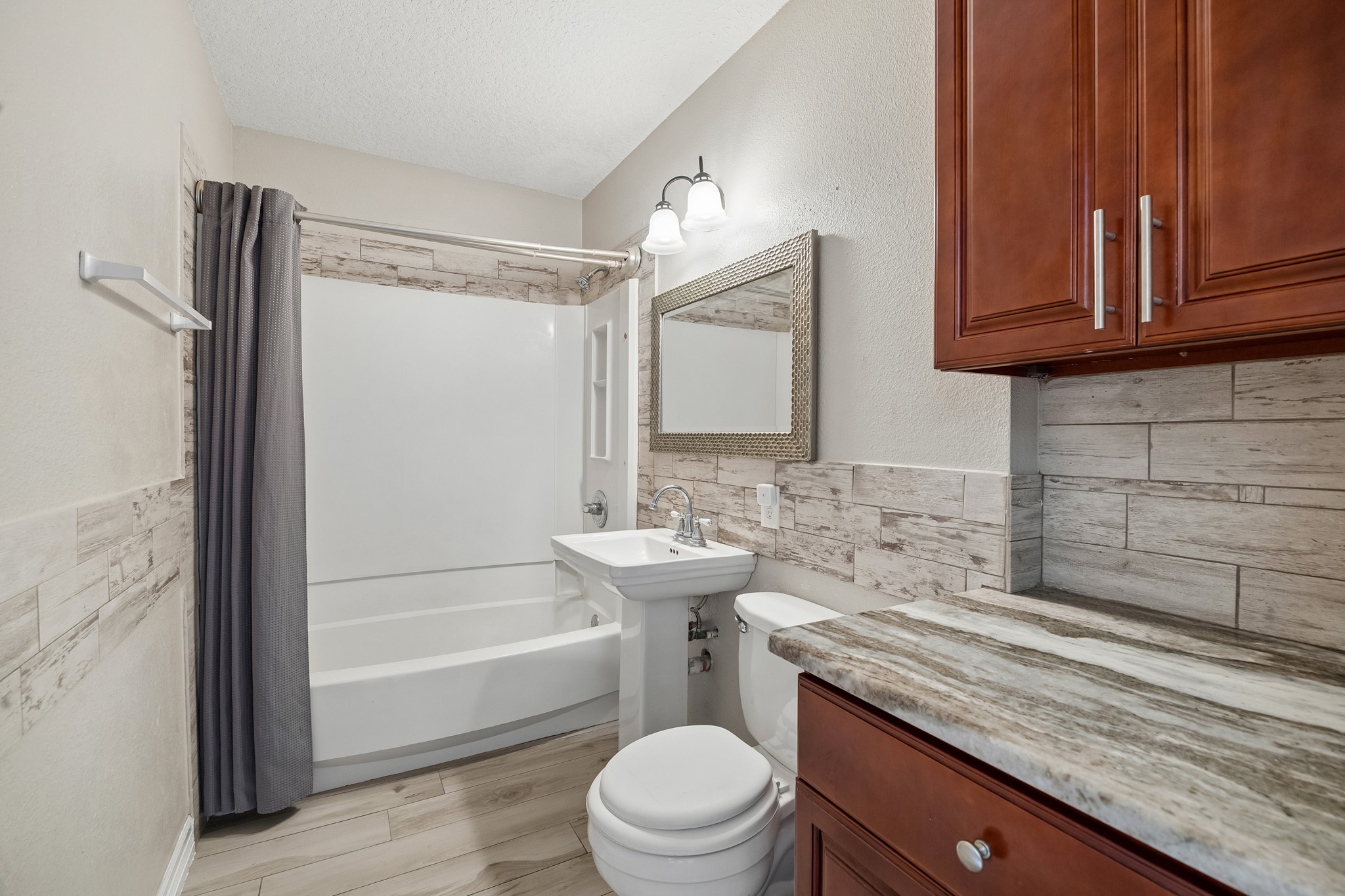Charming bathroom featuring a sleek pedestal sink, elegant tiled walls, and rich wood cabinetry, complemented by a modern shower and tub combination.