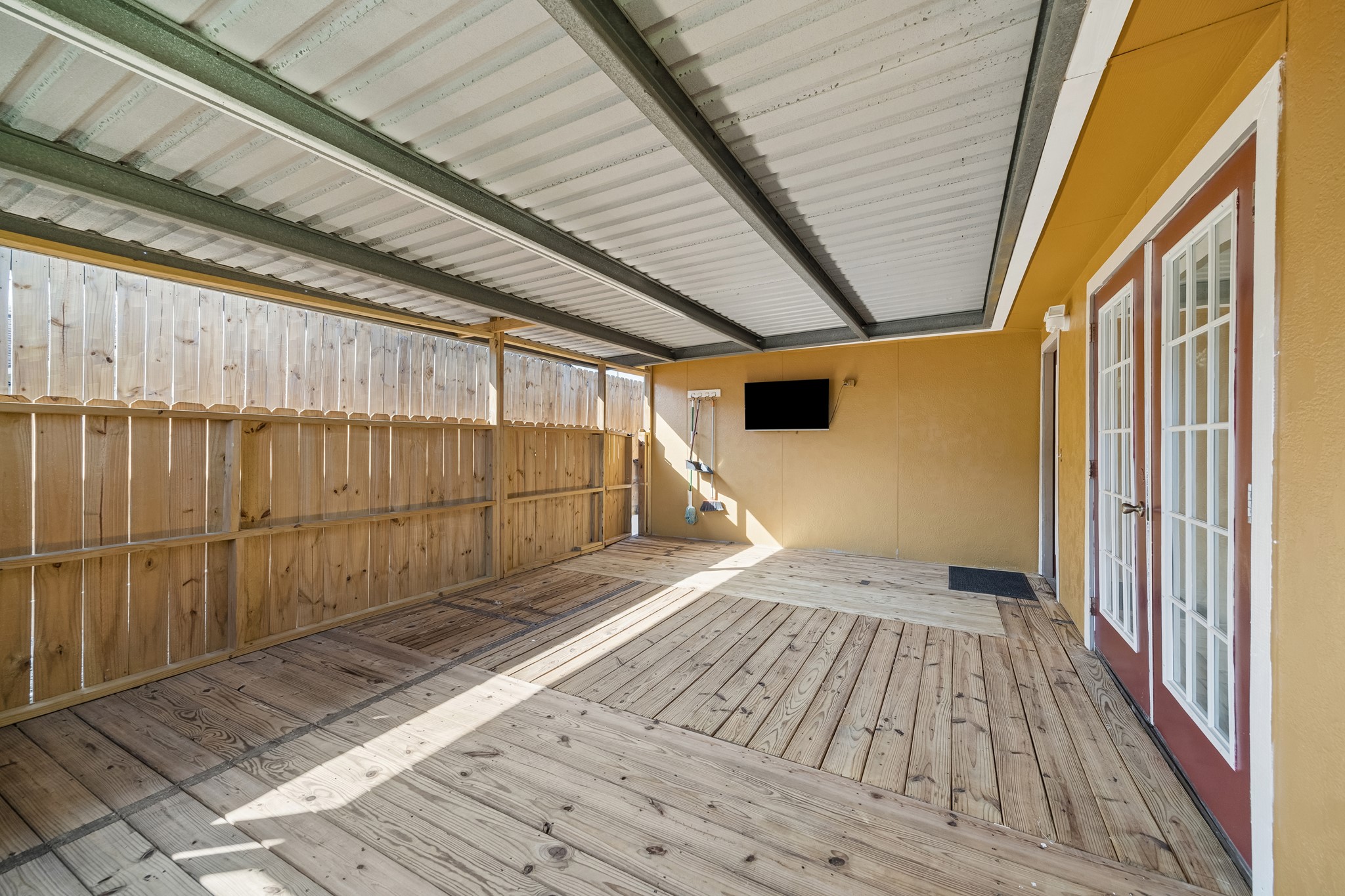 Spacious covered patio with wooden decking and French doors, perfect for outdoor relaxation and entertainment.