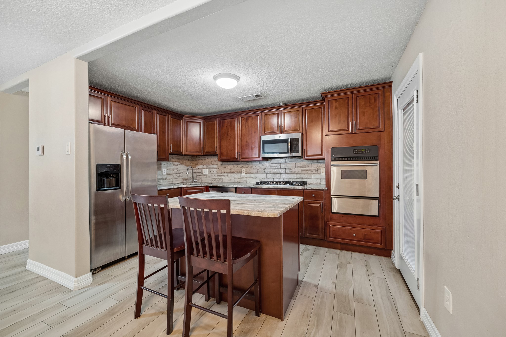 Elegant kitchen with rich wood cabinetry, a modern stainless steel refrigerator, and a built-in oven. The cozy island offers additional workspace and seating, perfect for casual dining.