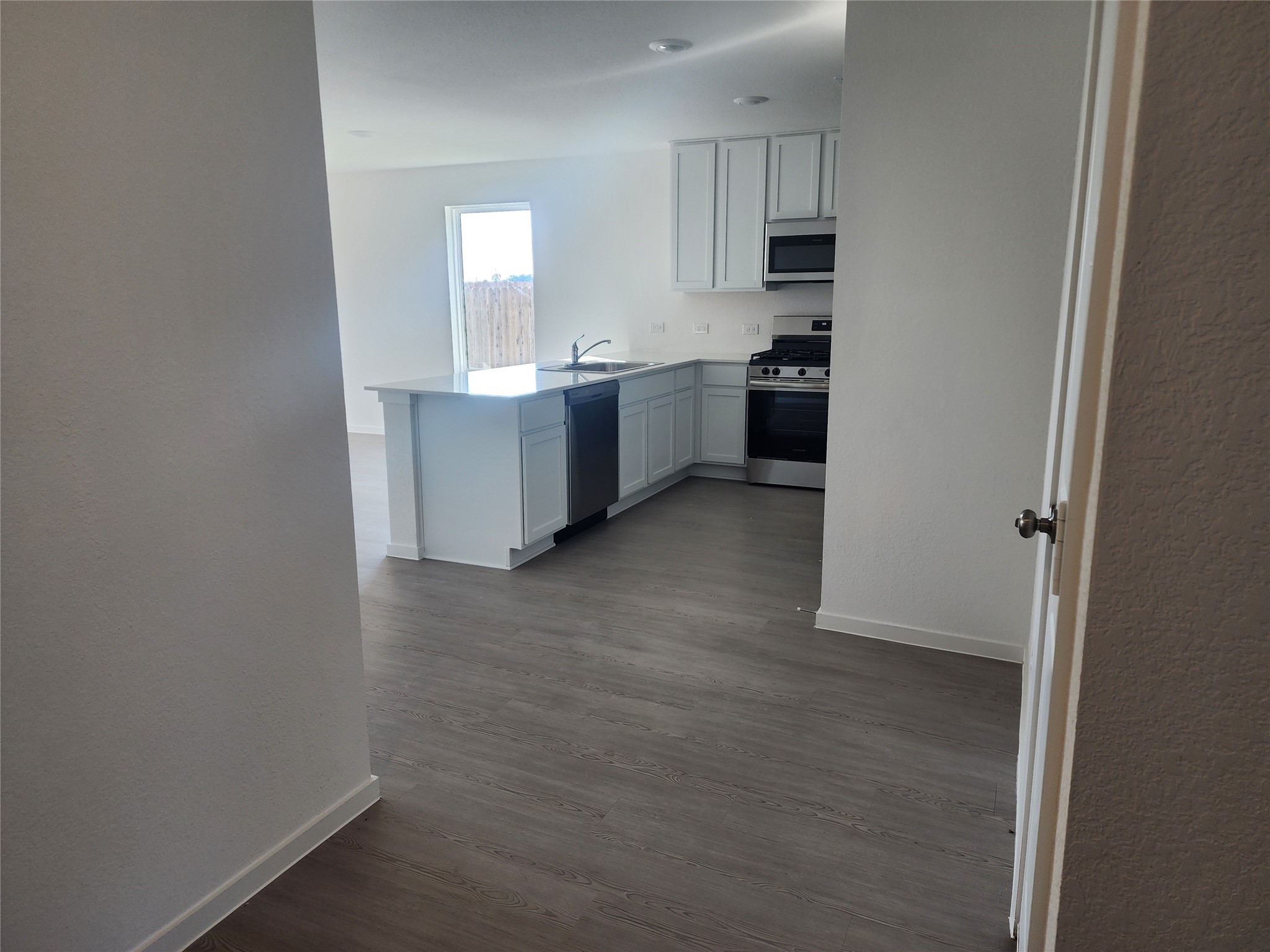 This photo showcases a modern, open kitchen with sleek white cabinetry, stainless steel appliances (included) from view of entryway hallway.