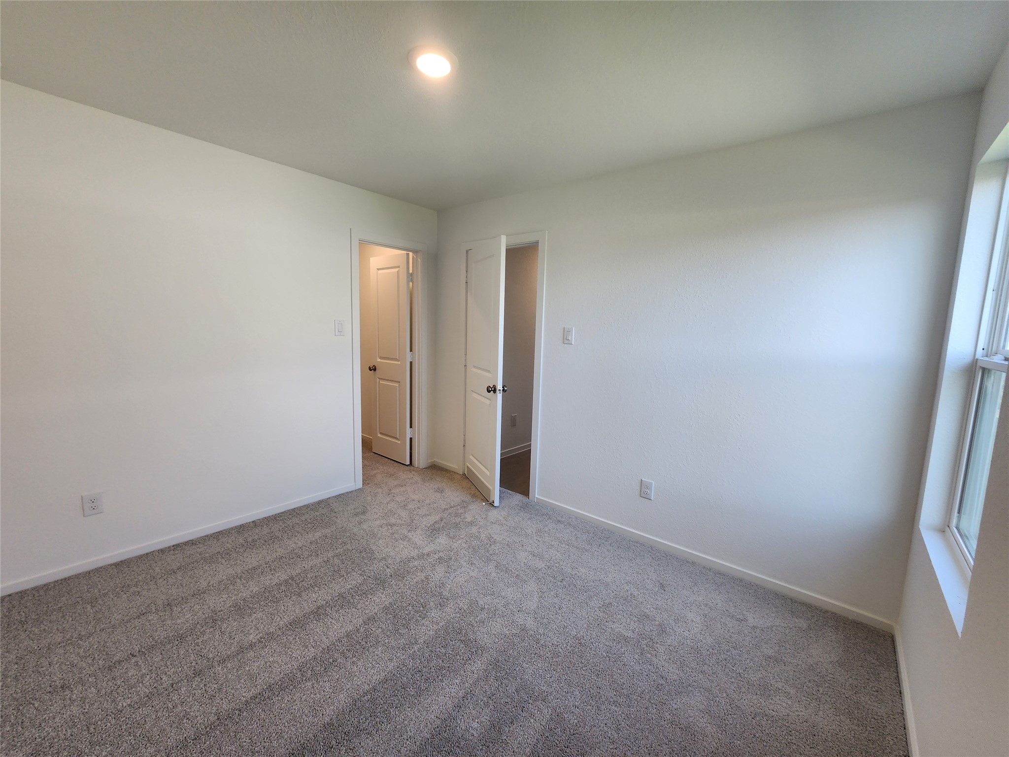 Secondary bedroom with walk-in closet features soft carpeting and a large window for natural light.