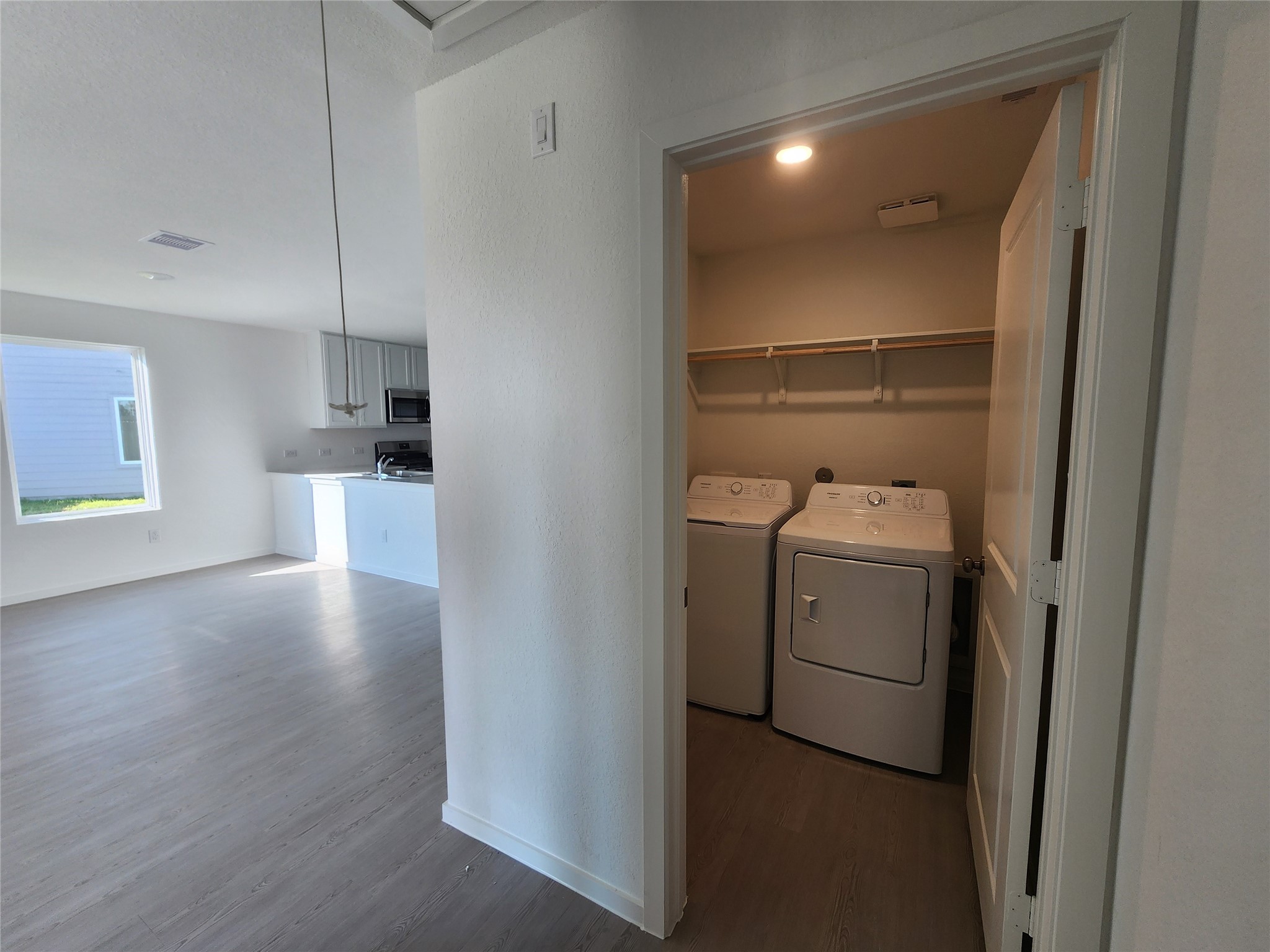 Bright, open living space with light wood flooring and a separate laundry room equipped with a washer and dryer located across from the primary bedroom.