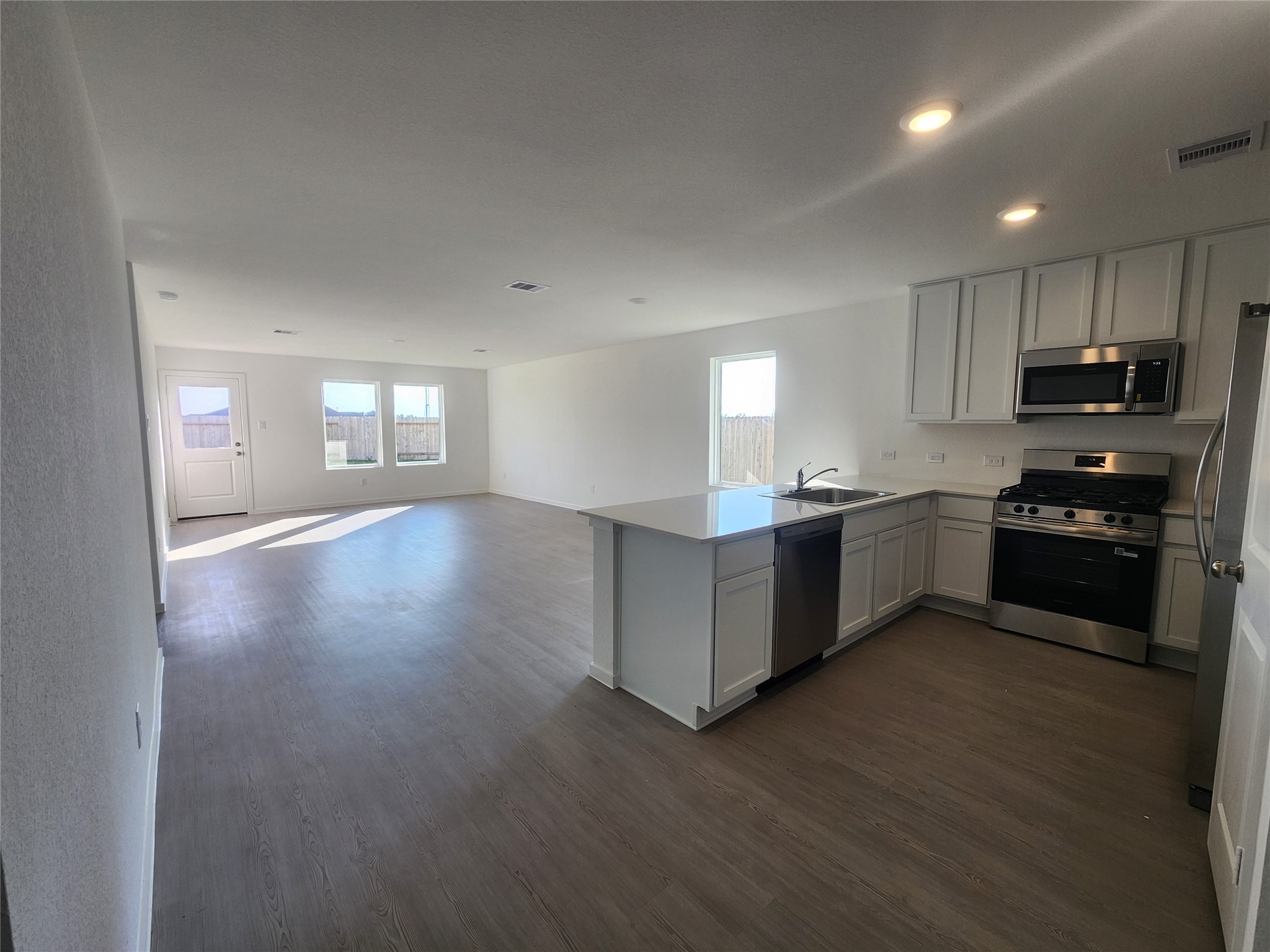 View of open-concept living/dinning space featuring a bright kitchen with stainless steel appliances and ample counter space. The adjoining living area is spacious with large windows and a door leading outside, providing plenty of natural light.
