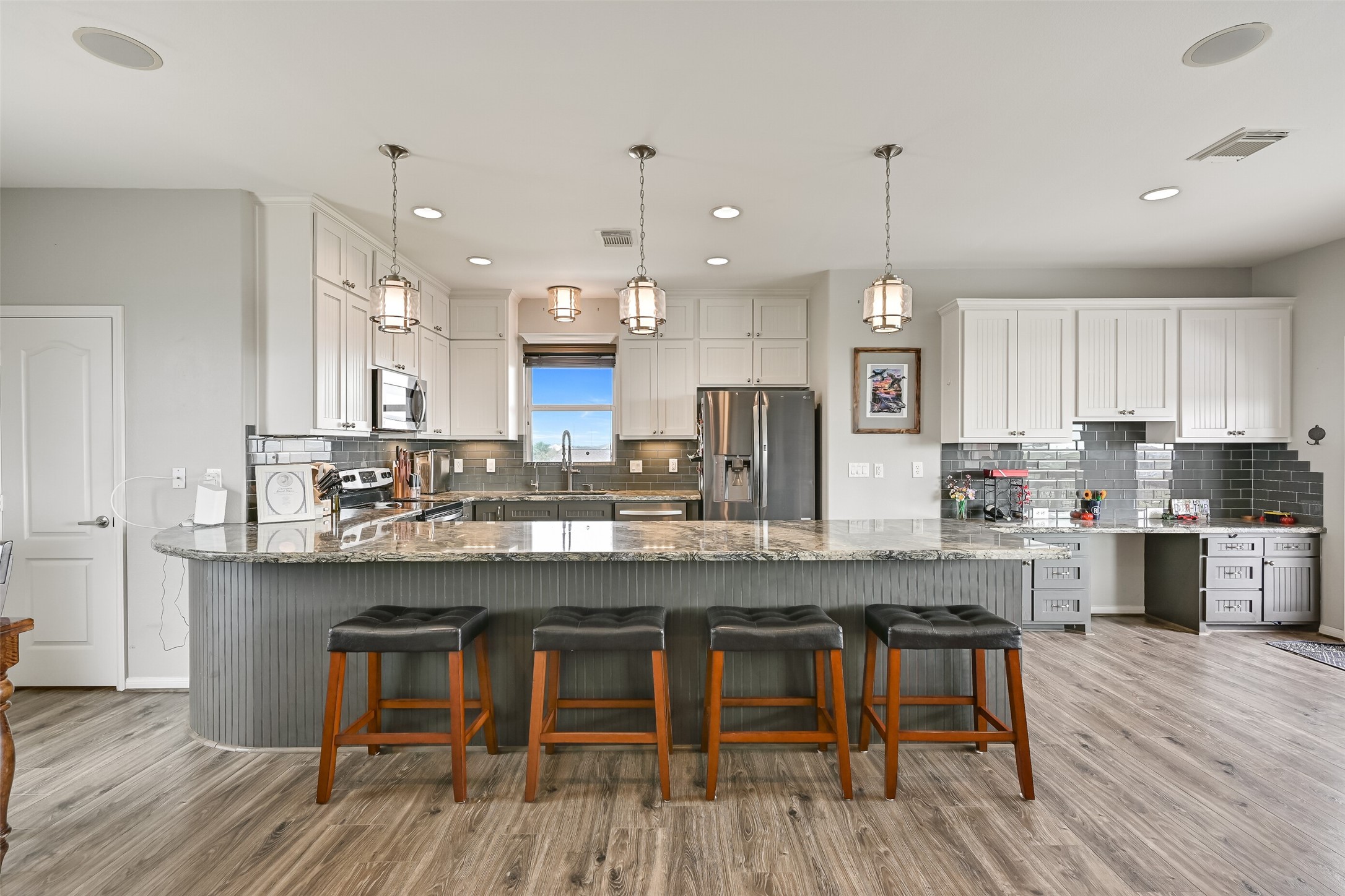 Notice the oversized peninsula island lathed in stunning silver cloud granite with a contrasting beadboard wall kick. The door to the Left reveals an oversized walk-in pantry.