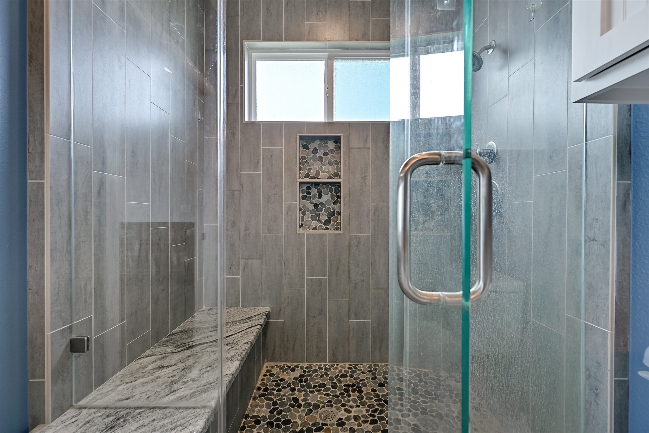 This spa-like walk in shower showcases a frameless glass enclosure, pebble floor, and convenient bench lathed with granite. Notice the double shower niches.
