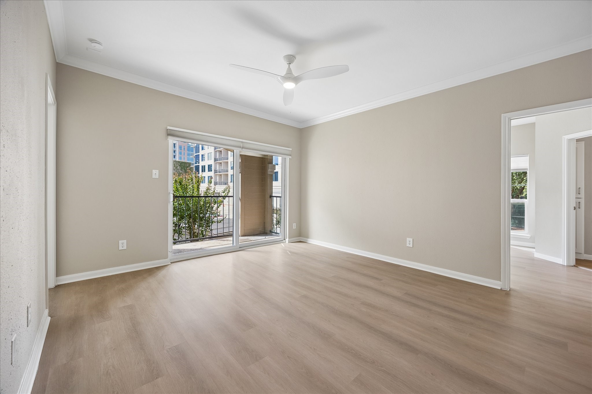 One more view of the large living room w/new LVT flooring throughout, crown molding & new ceiling fan w/ light. Large sliding glass doors fill the space w/ natural light & lead to the private covered balcony overlooking beautifully landscaped community grounds. Door to the right leads to the primary suite.