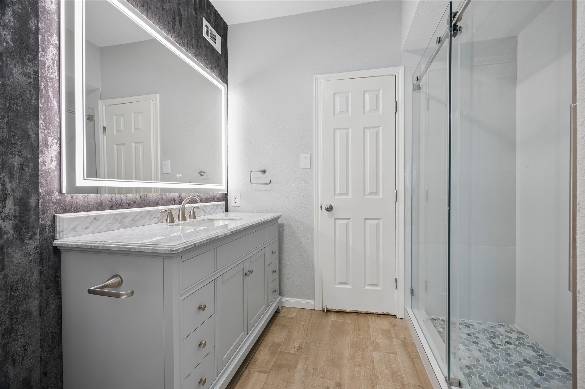 Beautifully extensively updated secondary bathroom featuring a vanity w/ a LED lighted vanity mirror. Notice the walk-in shower w/ frameless sliding glass door, handheld showerhead & hexagon tile flooring. Decorative accent wallpapered wall adds a stylish finishing touch!