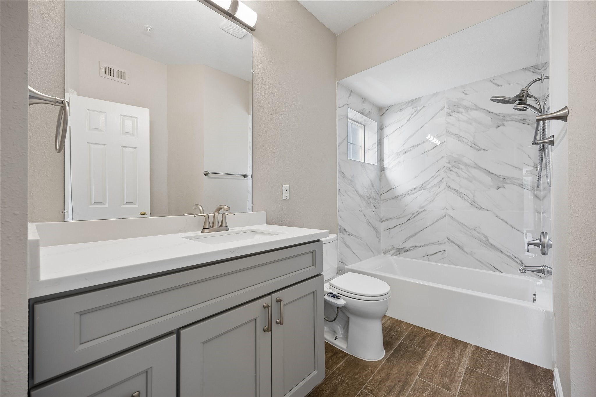 En-suite primary bathroom updated in 26, features a new vanity w/quartz countertop, ample cabinet storage, vanity mirror w/ overhead lighting & shower/tub combination w/new tub, new  tile surround & handheld showerhead. Additional features include new  tile flooring, built-in linen cabinet & window providing natural light.