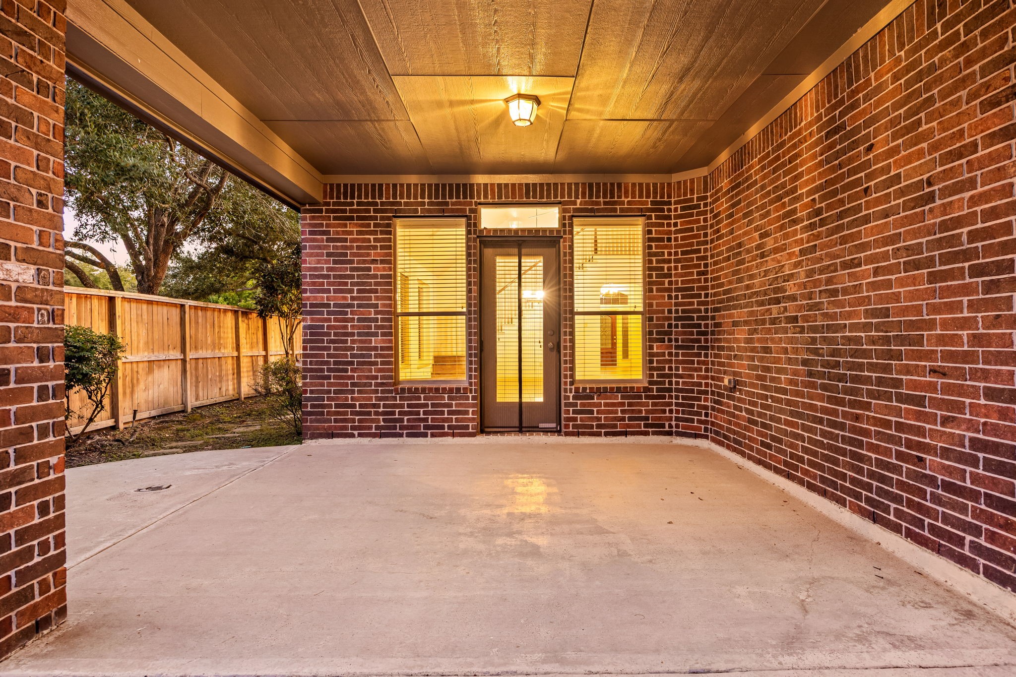 This expansive covered patio serves as a fantastic outdoor extension of the home, framed by a handsome, full-brick structural design and a high wood-paneled ceiling.