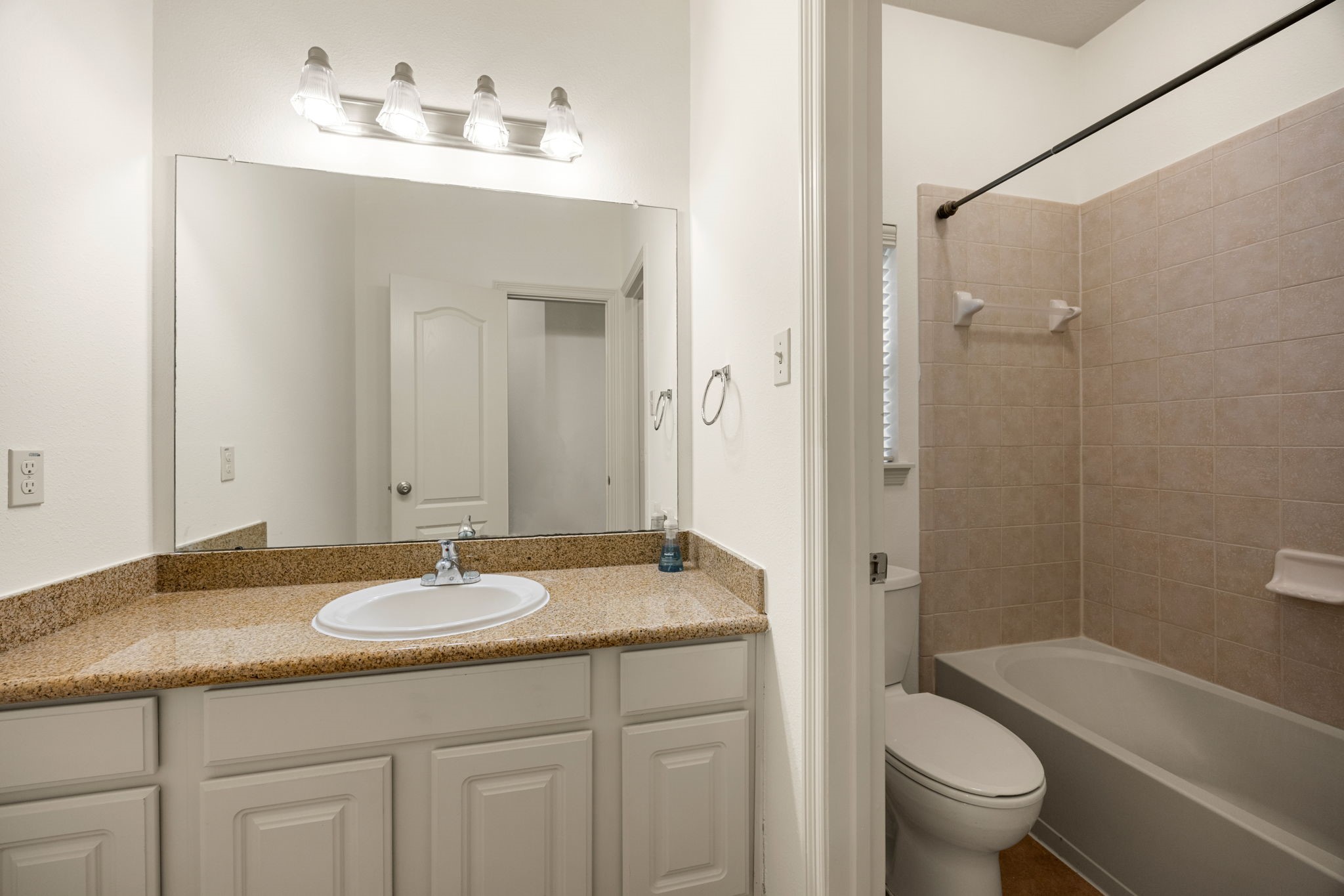 This secondary bathroom features a highly functional layout designed to streamline busy mornings, showcasing a white vanity with granite countertop, tub/shower combination with tile surround, and tile flooring.