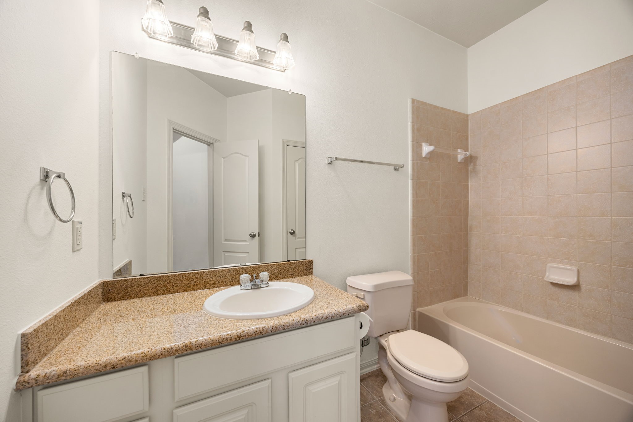 Conveniently located directly adjacent to the upstairs game room, this full secondary bathroom features a highly functional layout anchored by a spacious single vanity with neutral granite countertops.