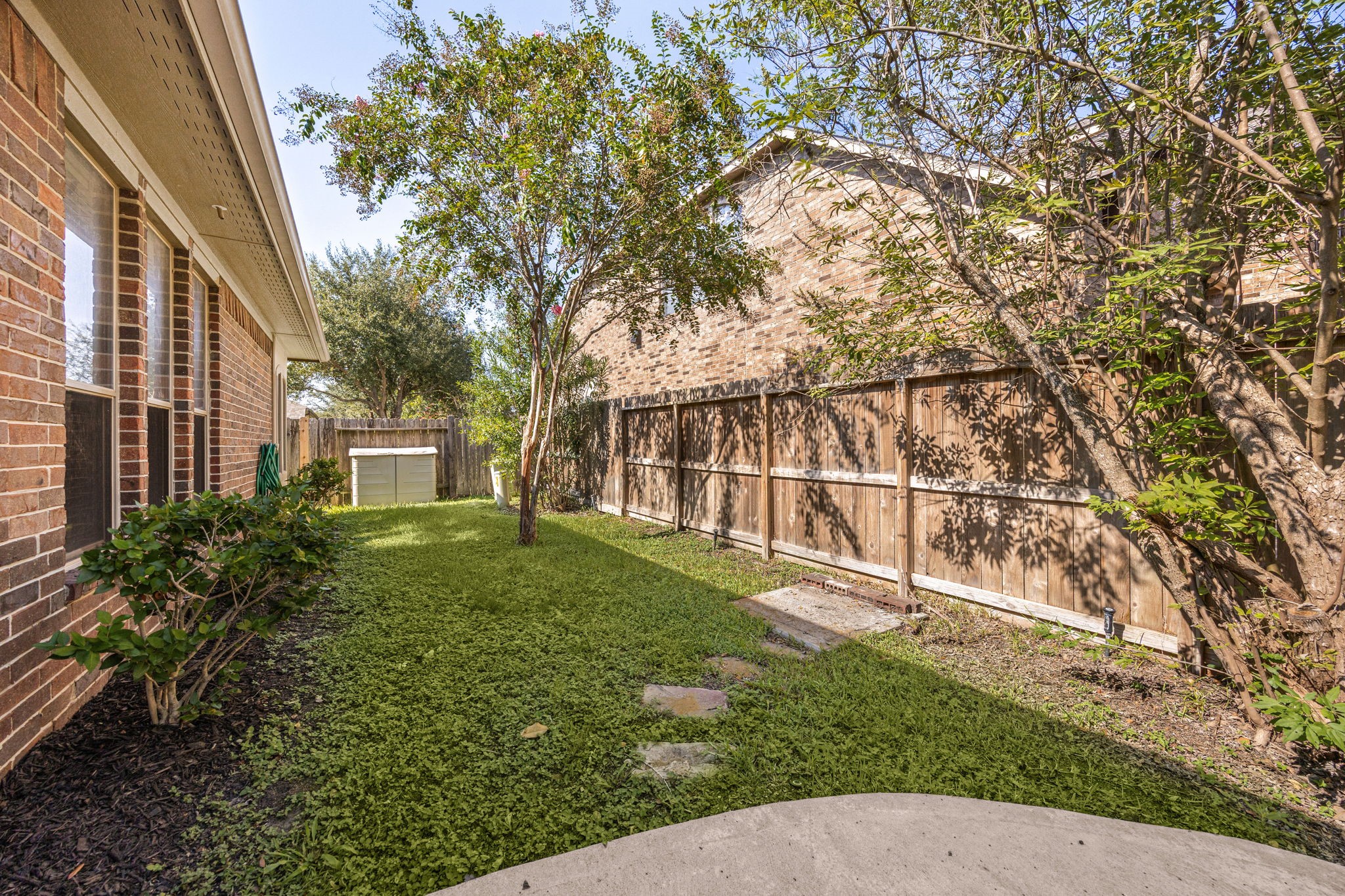 This side view of the backyard highlights a beautifully shaded green space and a secure wooden privacy fence.