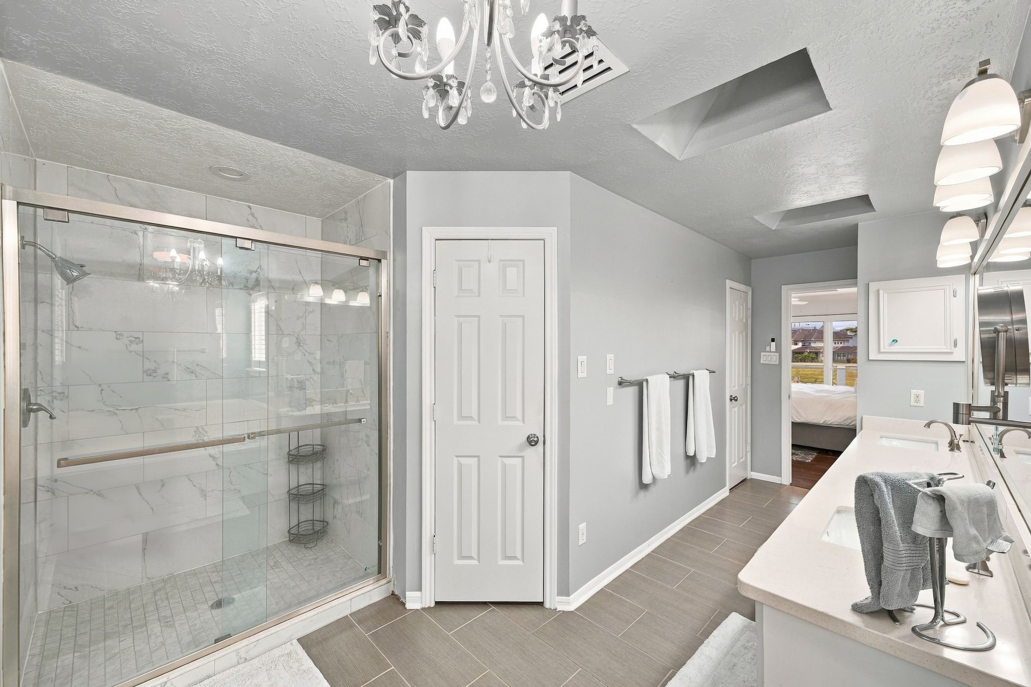 The primary bath has a separate glass-enclosed shower, a chandelier, and an arched window.