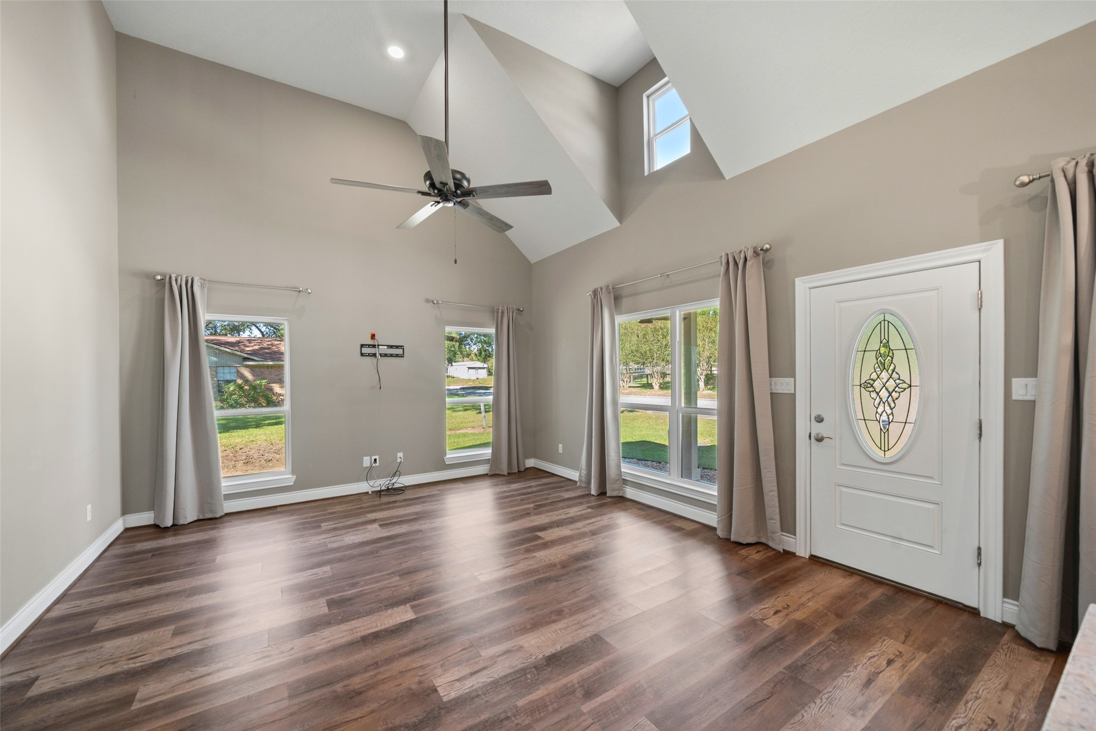 Living area featuring a high ceiling, ceiling fan, wood-look flooring, and double entry doors with decorative glass.