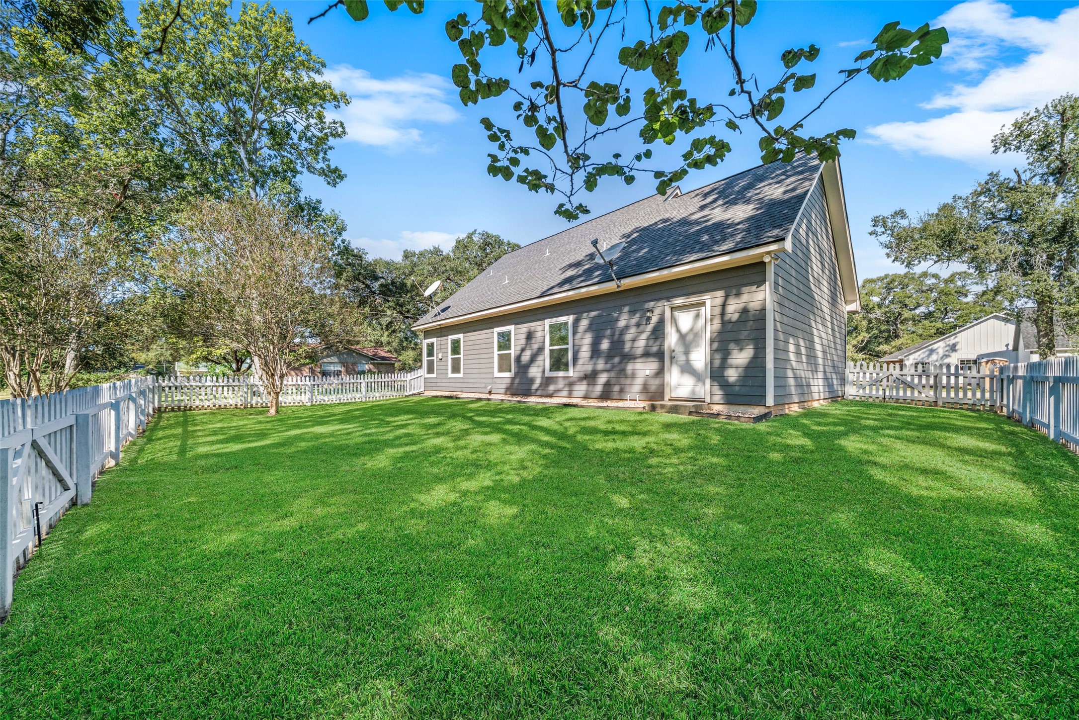 Additional backyard view highlighting the homes stone exterior, fenced lawn, and mature trees.