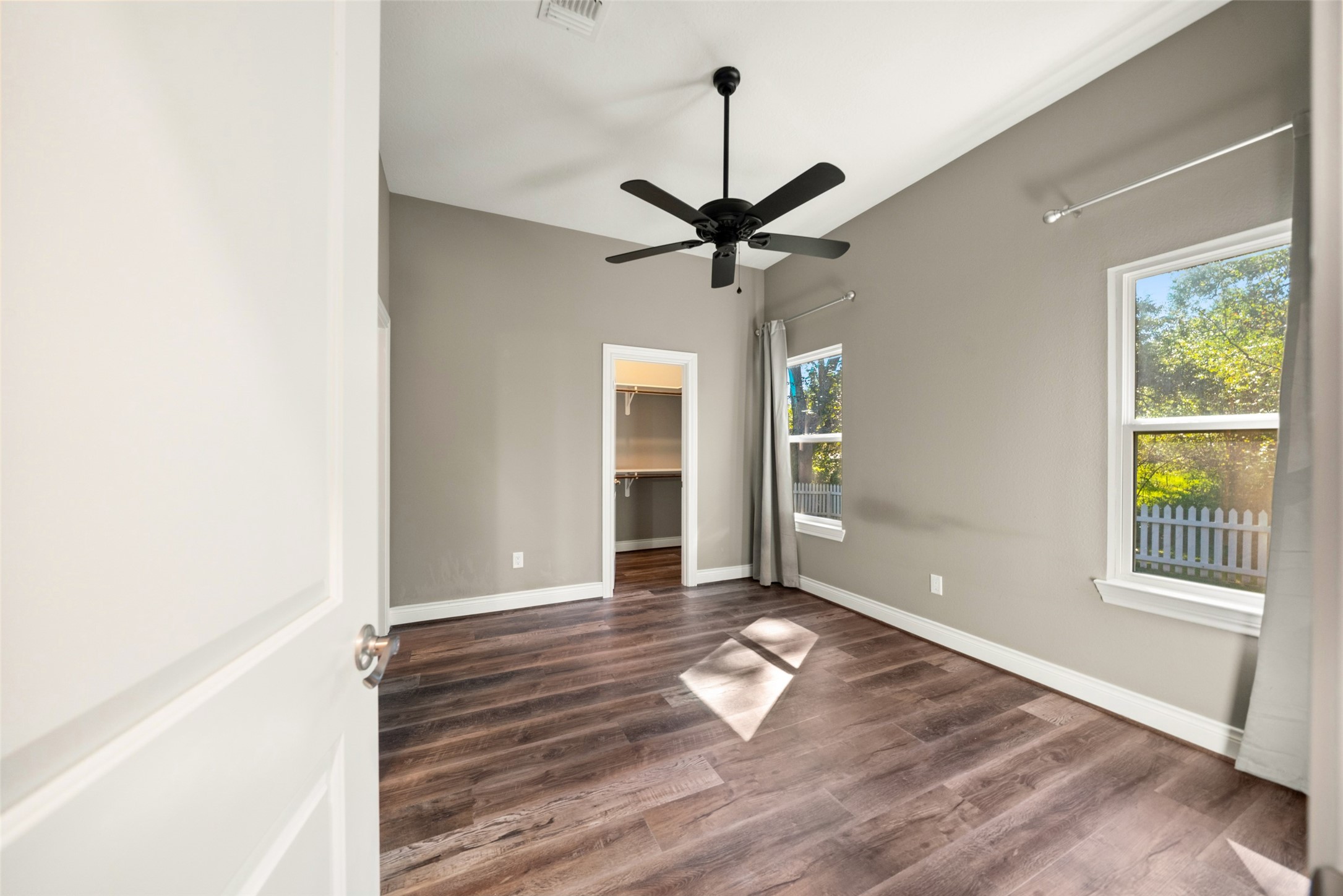 Bedroom featuring wood-look flooring, a ceiling fan, neutral walls, and natural light from two windows.