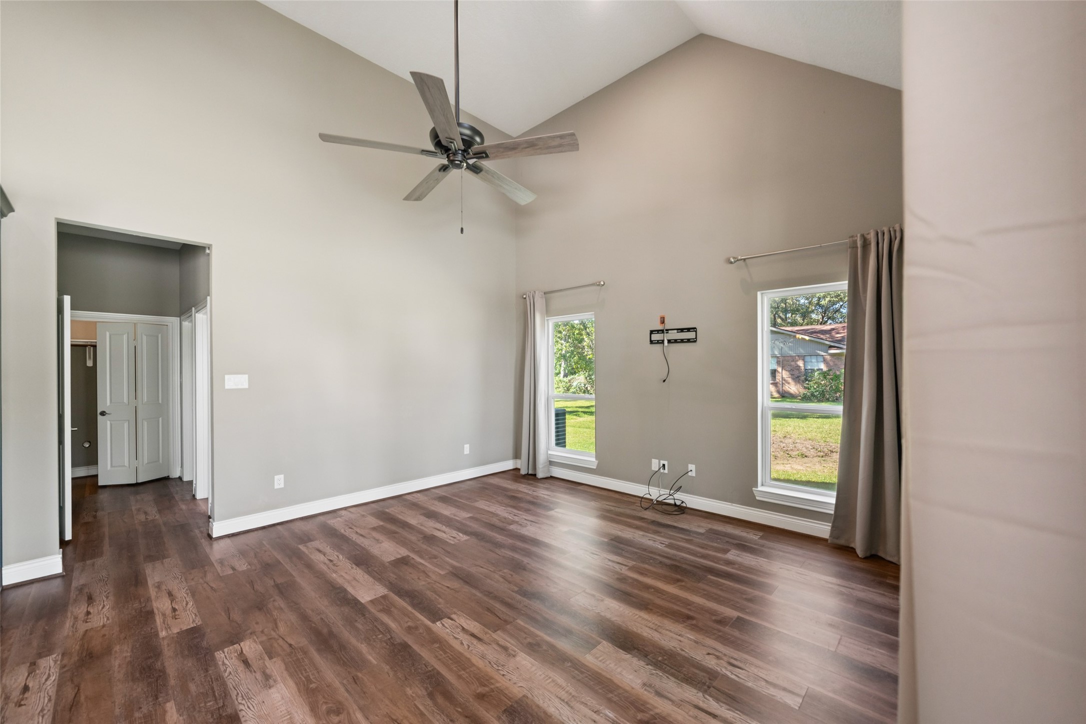 Living area featuring a vaulted ceiling, ceiling fan, wood-look flooring, and multiple windows for natural light.