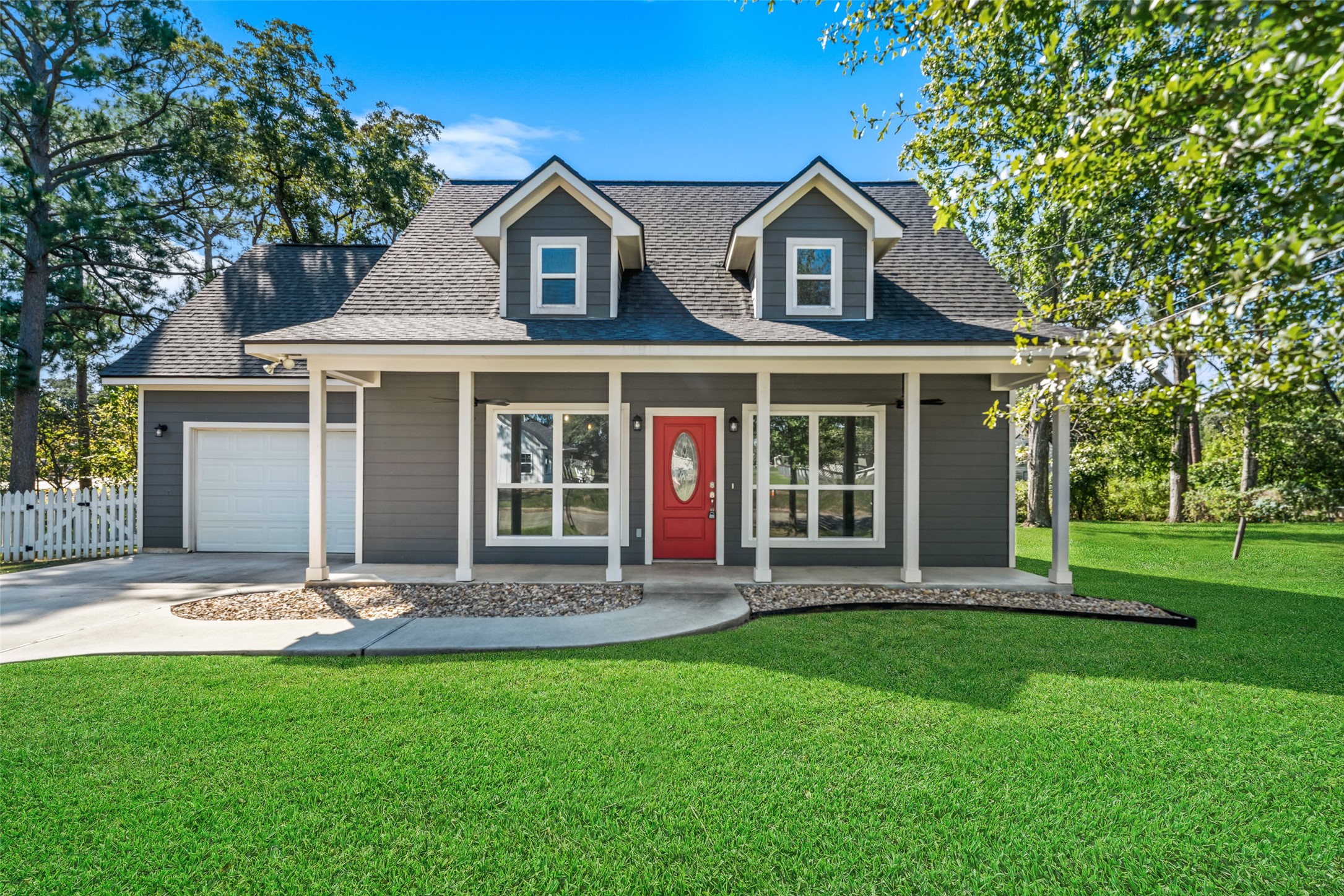 Front exterior featuring an attached garage, covered porch with white columns, and a spacious lawn.