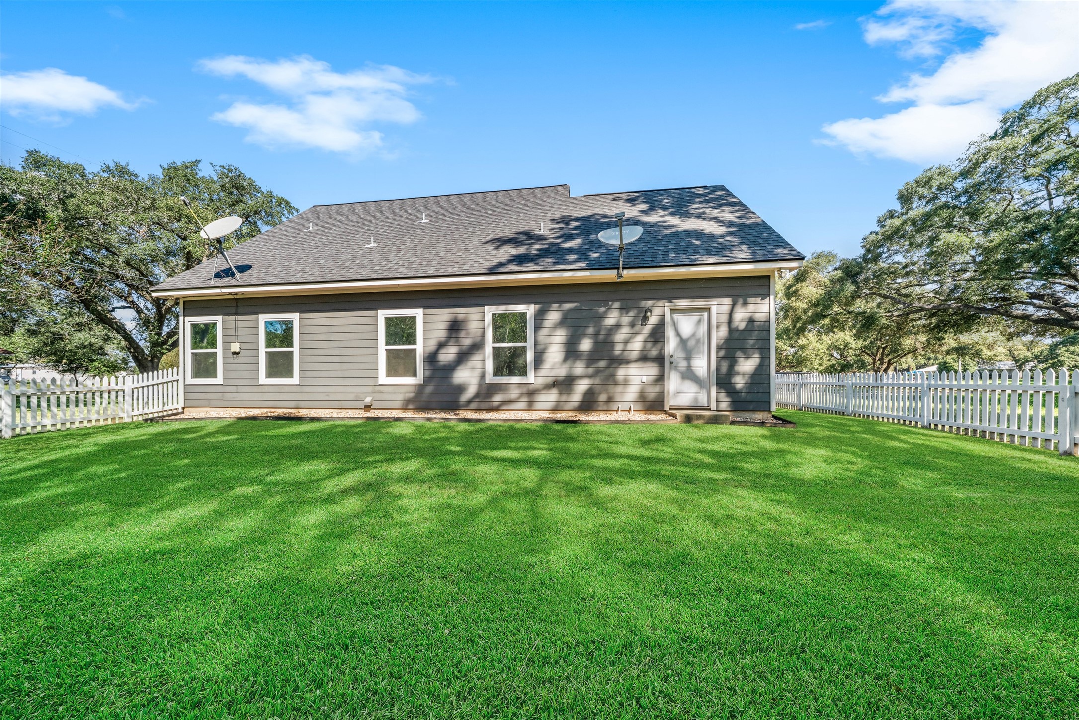 1. Backyard view featuring the homes stone exterior, spacious lawn, and mature shade trees.