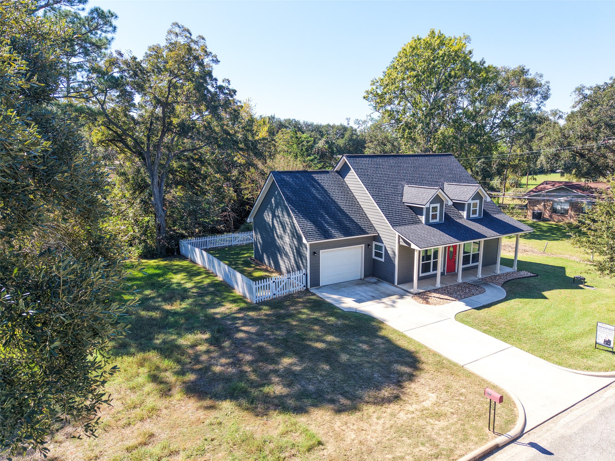 Elevated front view showcasing the covered porch, attached garage, concrete driveway, and mature shade trees.