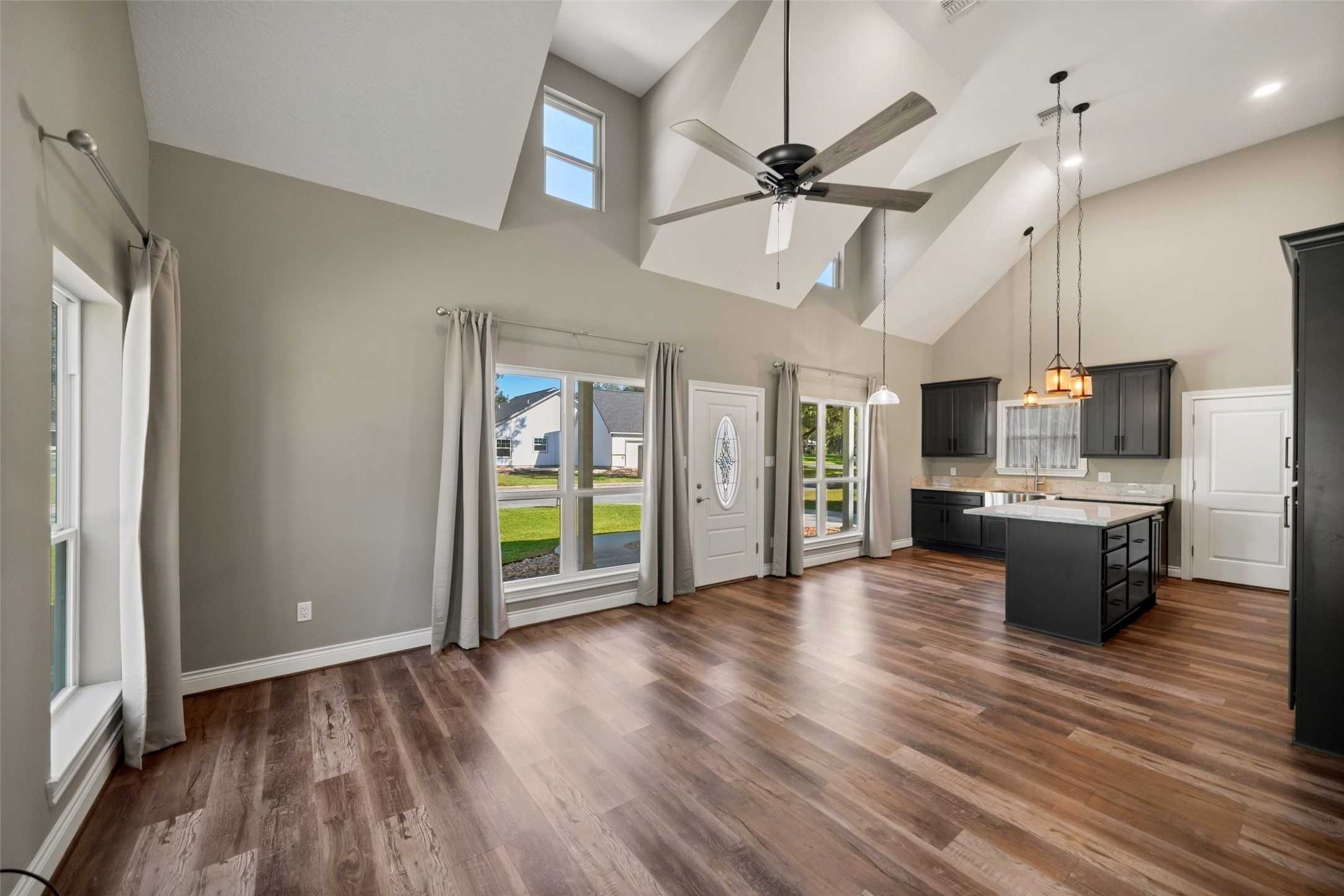 Spacious living area featuring a vaulted ceiling, upper accent windows, and an adjoining island kitchen.