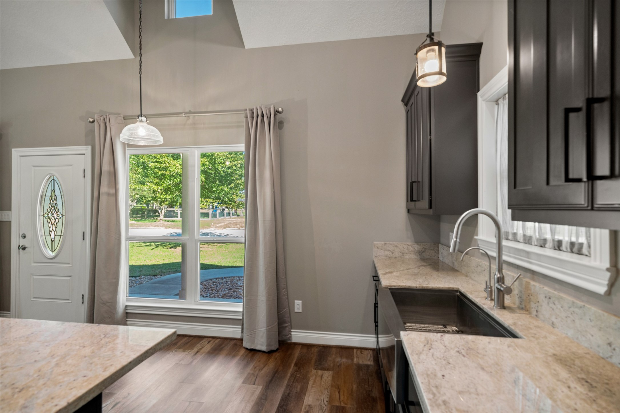 Kitchen view highlighting dark cabinetry, light countertops, pendant lighting, and adjacent windows overlooking the yard.