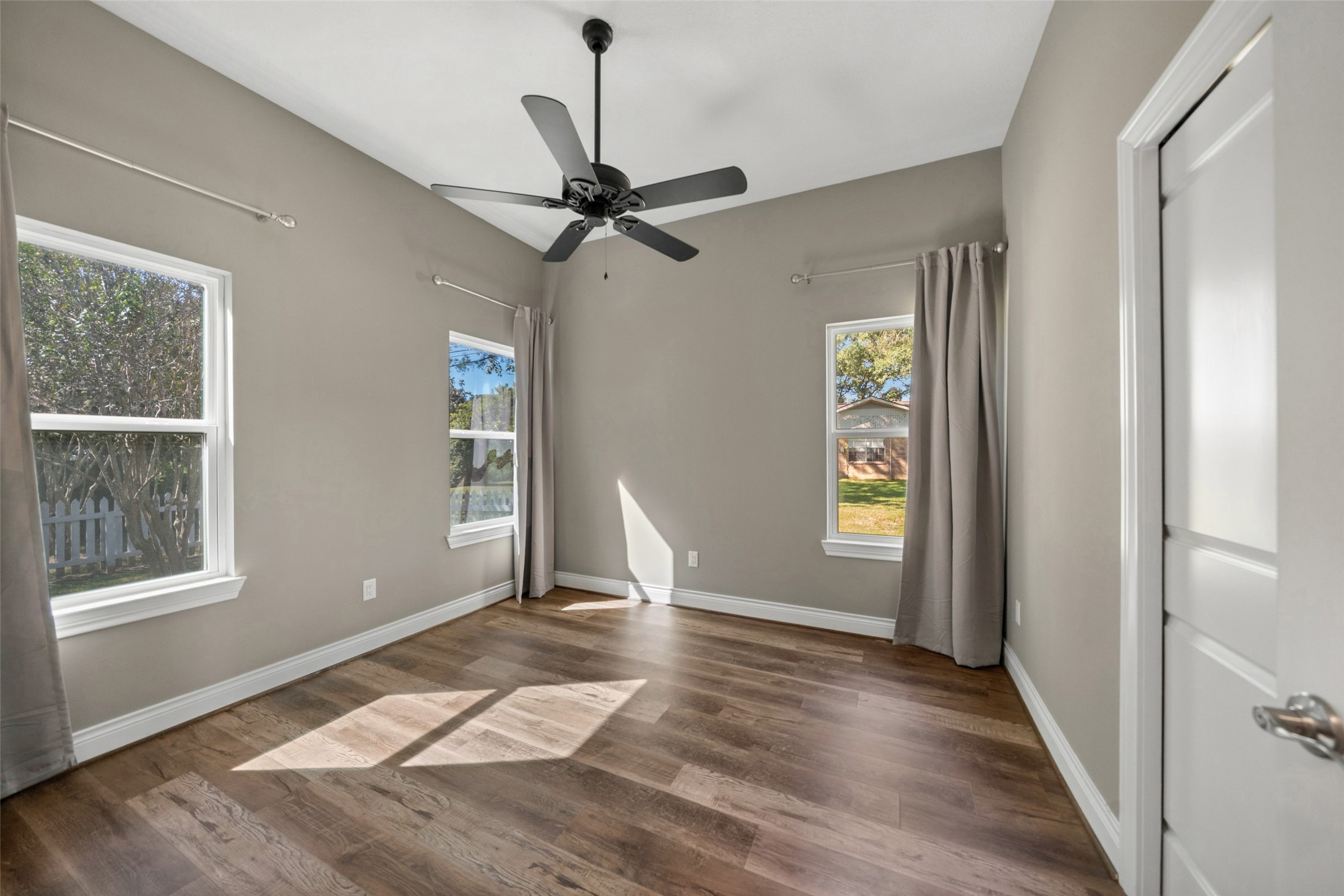 Bedroom featuring a tray ceiling, ceiling fan, wood-look flooring, multiple windows, and closet access.