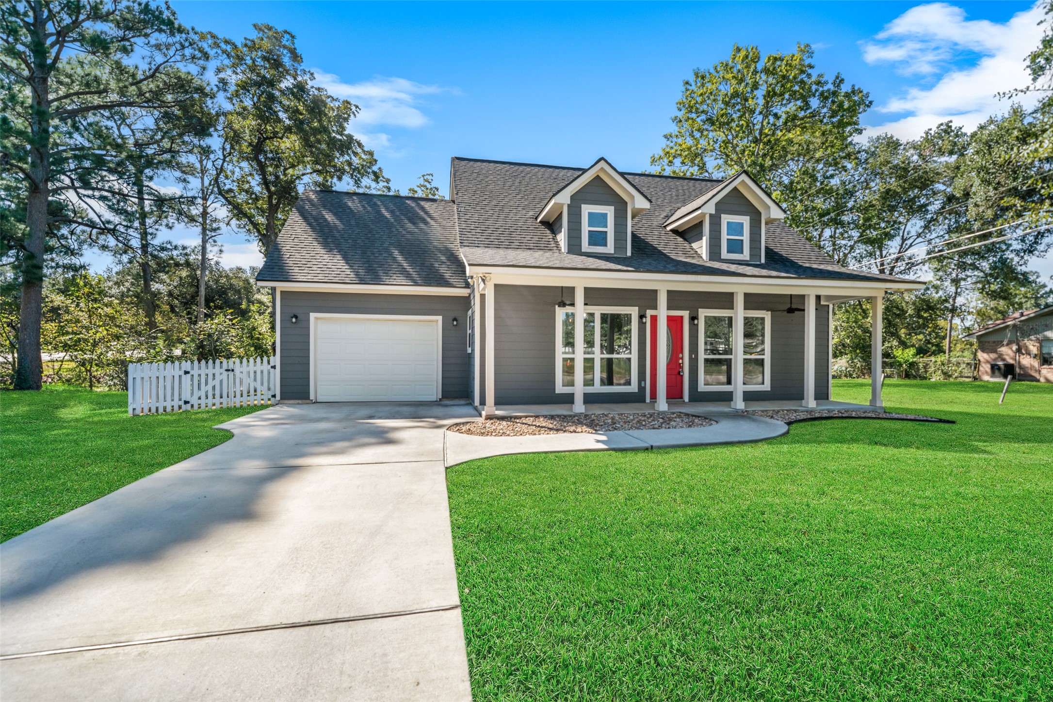 Wide front view showcasing the concrete driveway, attached garage, and home framed by established trees.