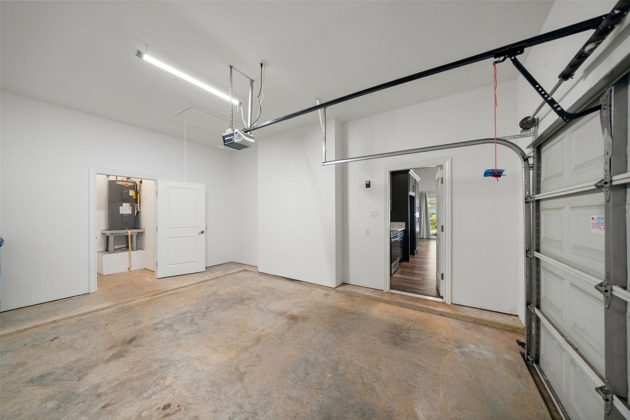 Garage featuring a concrete floor, overhead door with opener, and a water heater.