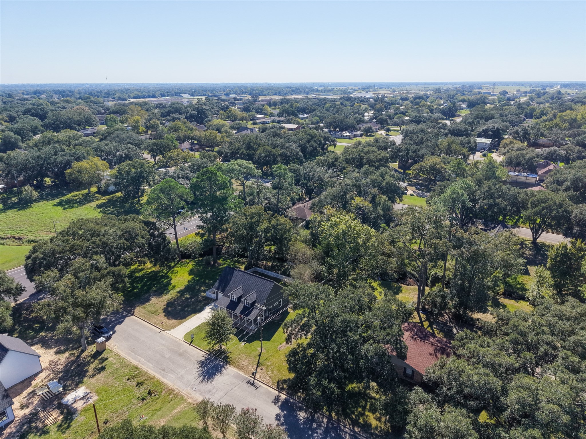 Wide aerial perspective highlighting the wooded surroundings and neighborhood beyond the home.