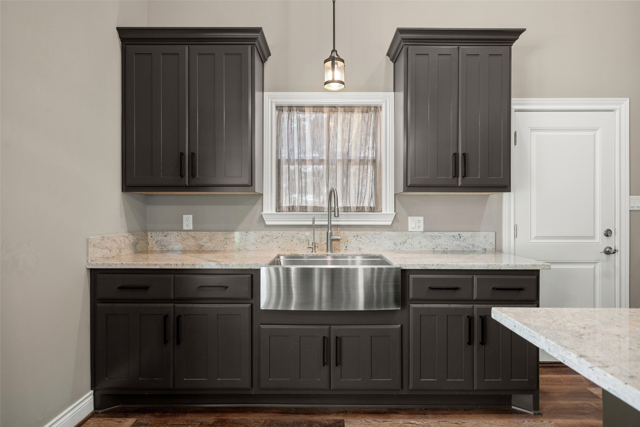Kitchen detail featuring dark cabinetry, light countertops, a stainless steel apron-front sink, and pendant lighting.