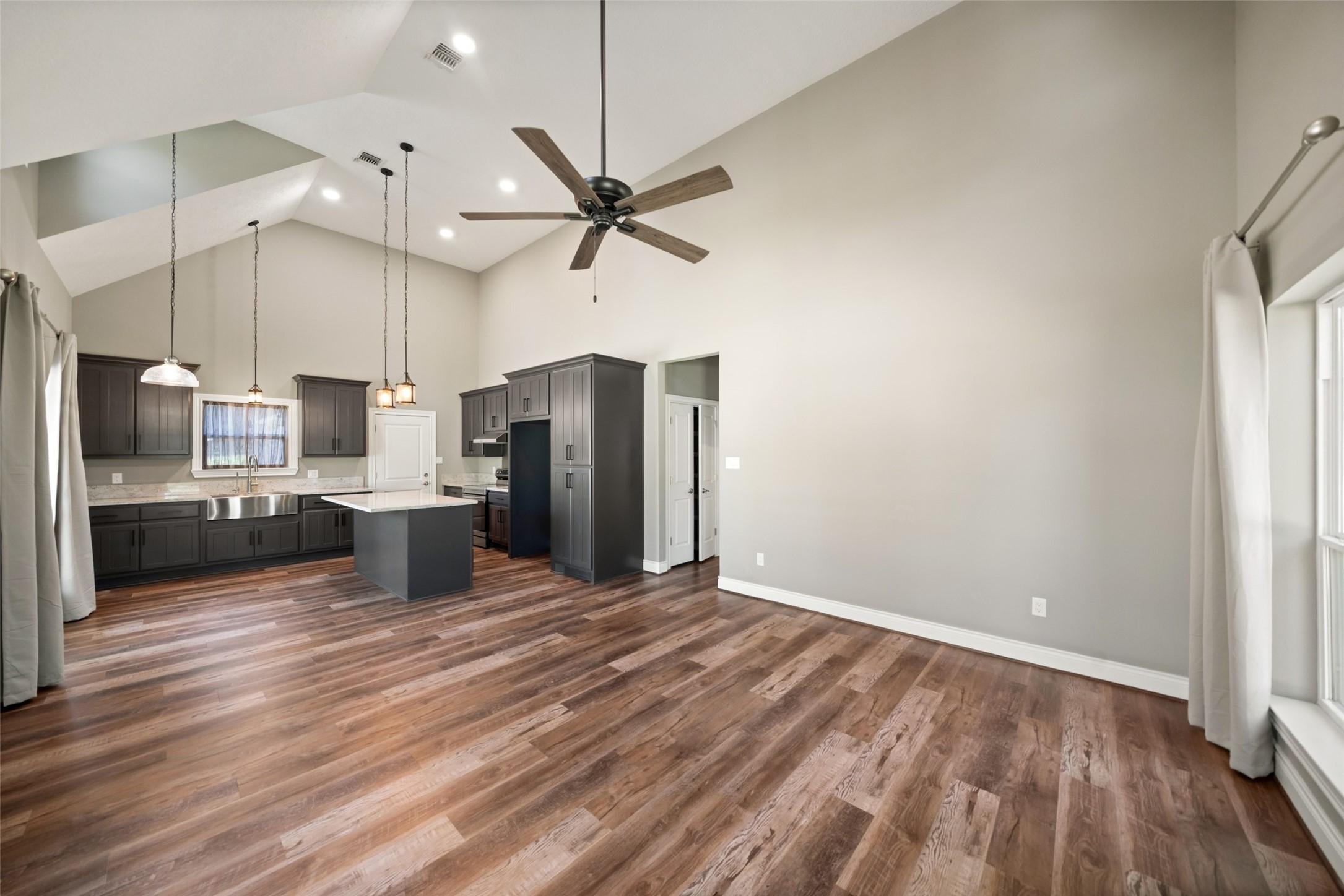 Open living and kitchen area with wood-look flooring, a ceiling fan, and recessed lighting.