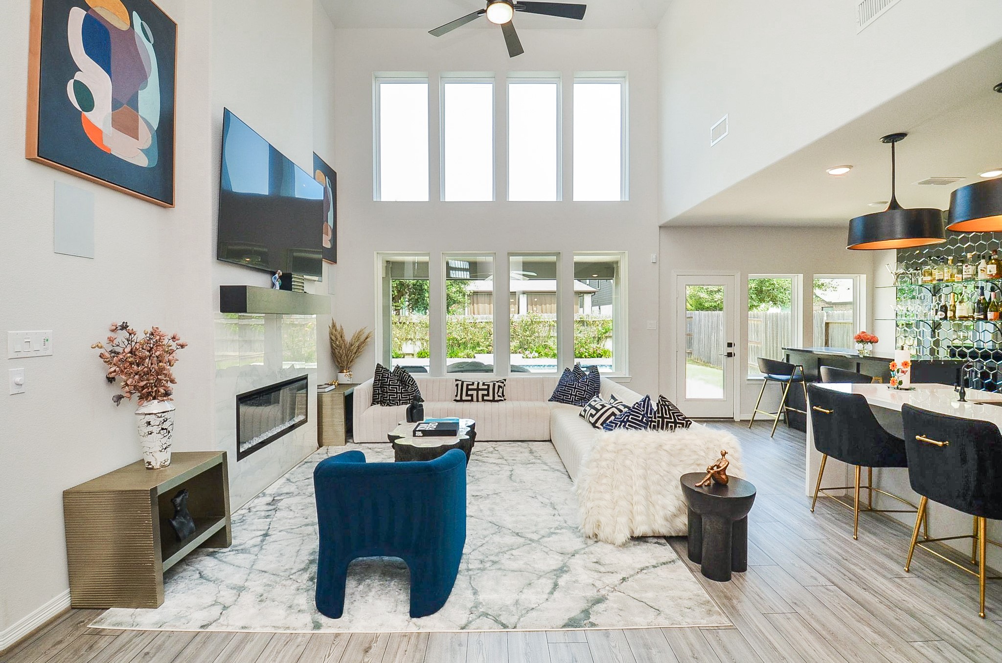 Stunning open-concept living area with soaring ceilings, abundant natural light, and a sleek modern design. The space features a cozy fireplace, elegant furnishings, and a stylish bar area perfect for entertaining.