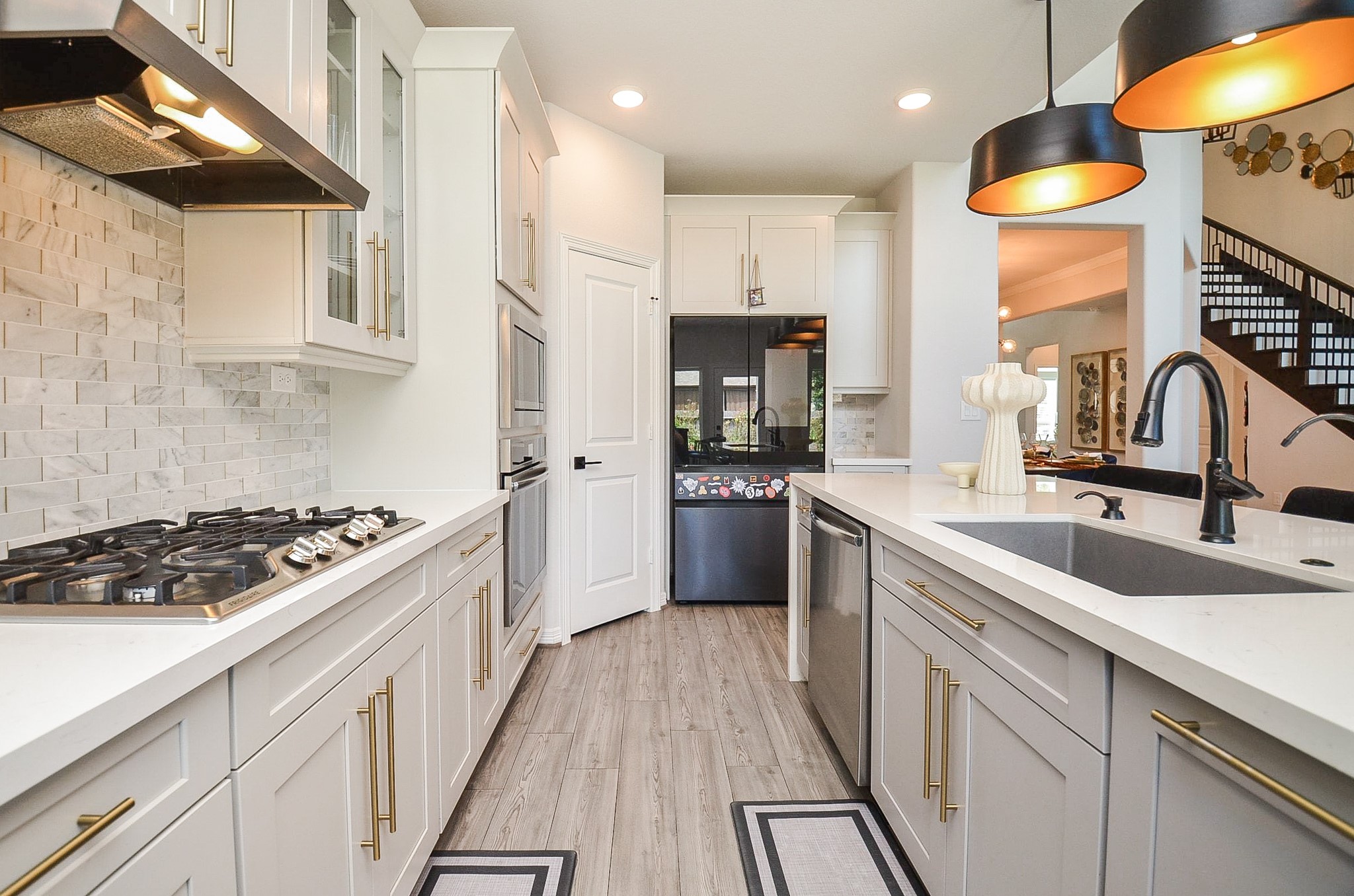 Sleek modern kitchen featuring elegant cabinetry, a spacious island with a sink, stylish pendant lighting, and a high-end stovetop, all accentuated by a chic tile backsplash.