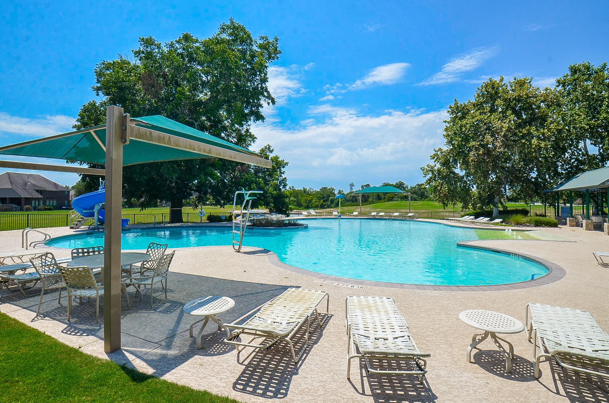 Experience relaxation at this inviting outdoor pool, complete with shaded seating, lush greenery, and a fun water slide.