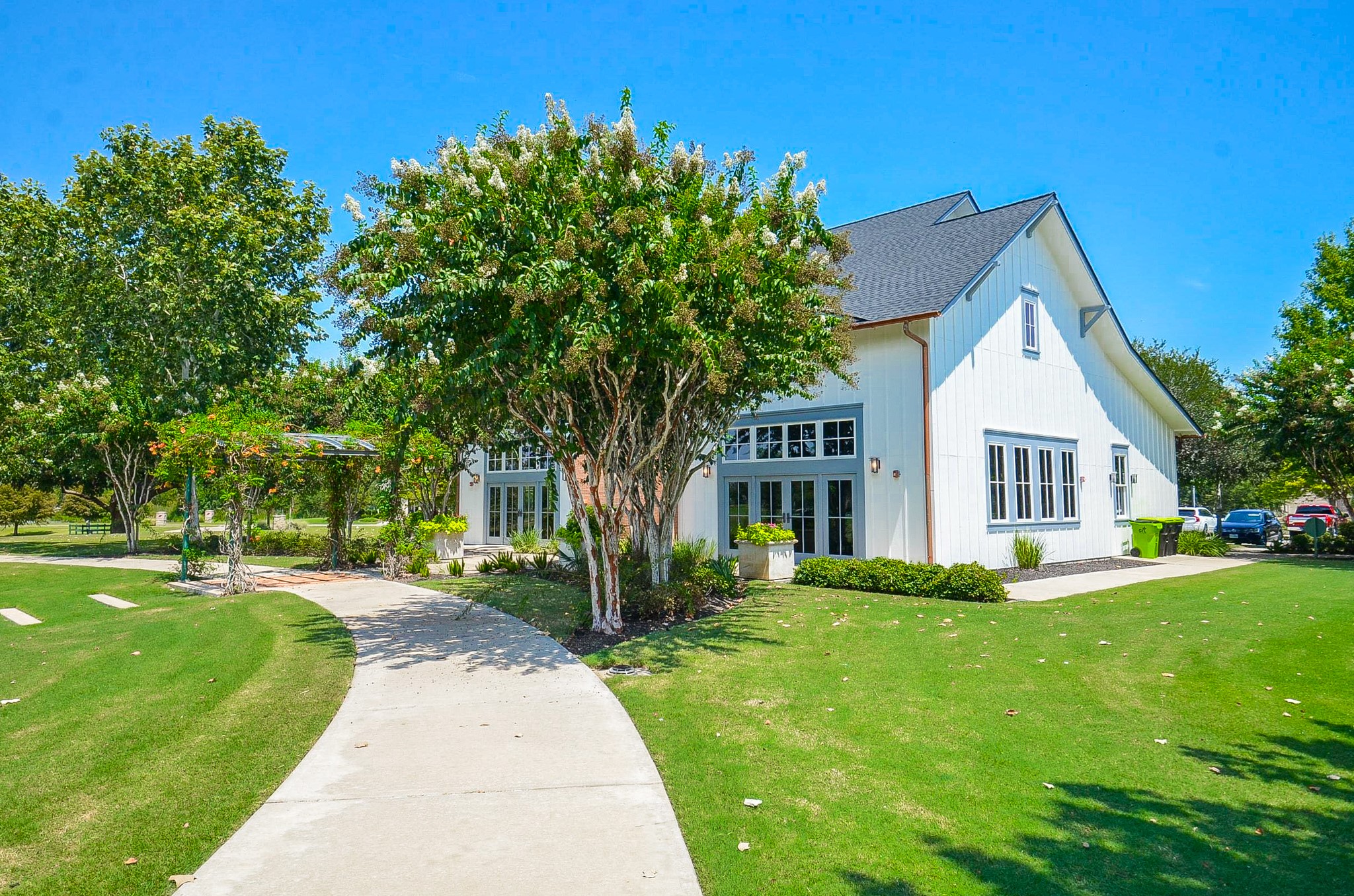 Charming modern farmhouse with crisp white siding and a beautifully manicured lawn, surrounded by lush trees and a welcoming pathway.